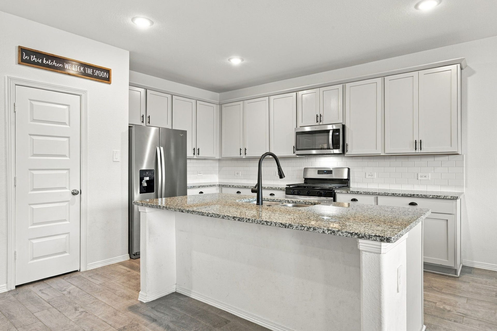 14424 Sunny Bend Way, Conroe, TX 77303 This bright and spacious kitchen features a modern, functional layout, beautiful speckled granite countertops, and a classic white subway tile backsplash. A generously sized center island offers ample preparation space, an integrated undermount sink, and a sleek black gooseneck faucet. Stainless steel appliances, including a French-door refrigerator, gas range, and built-in microwave, complement the kitchen's clean, contemporary finishes.