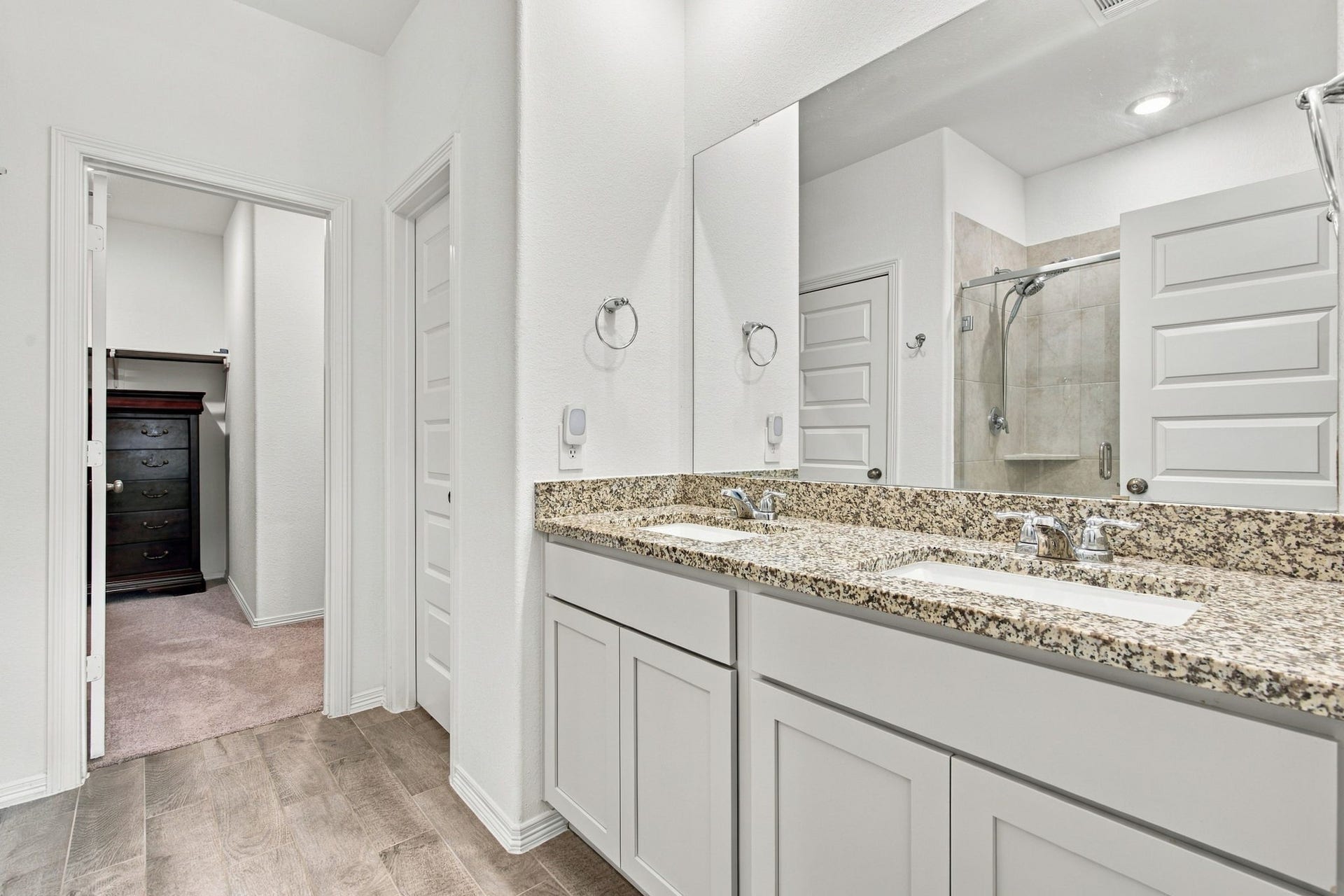 14424 Sunny Bend Way, Conroe, TX 77303 This bright and spacious primary bathroom features a beautiful double-sink vanity with speckled granite countertops, crisp white cabinetry, and chrome fixtures. A large wall-mounted mirror enhances the open feel of the space, while recessed ceiling lighting provides excellent illumination.