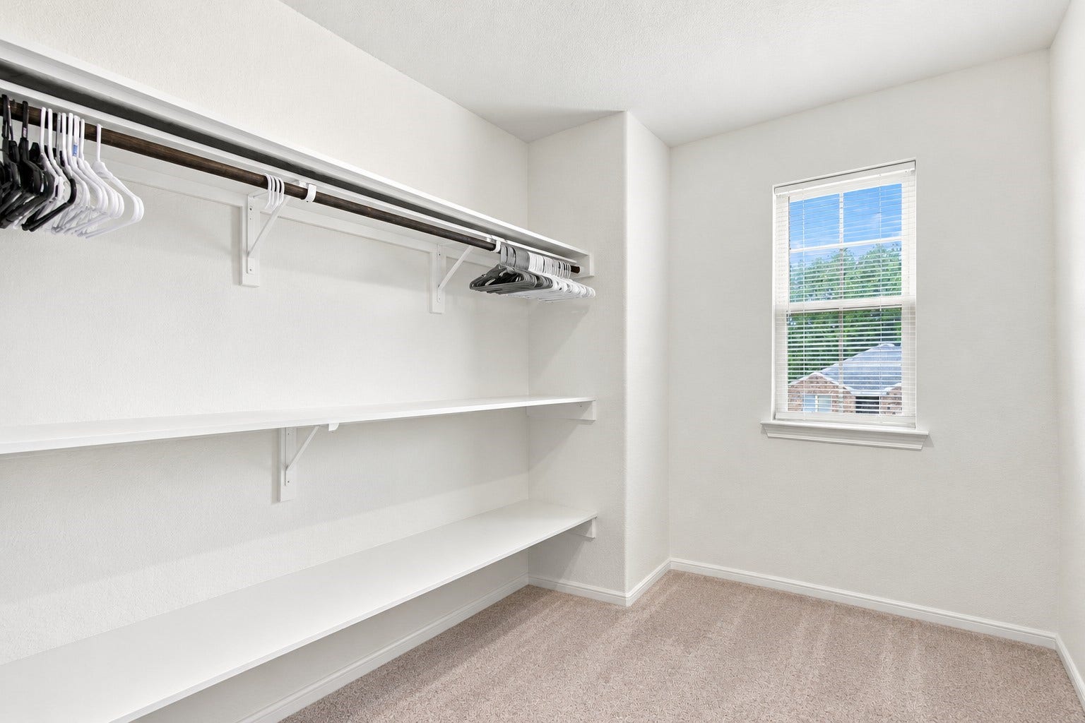 14424 Sunny Bend Way, Conroe, TX 77303 Virtually Arranged: This spacious walk-in closet features a bright, clean design with crisp white walls, soft neutral carpeting, and an abundance of natural light. Built-in white shelving provides generous storage and organization space, complemented by extended hanging rods with ample room for clothing and accessories.