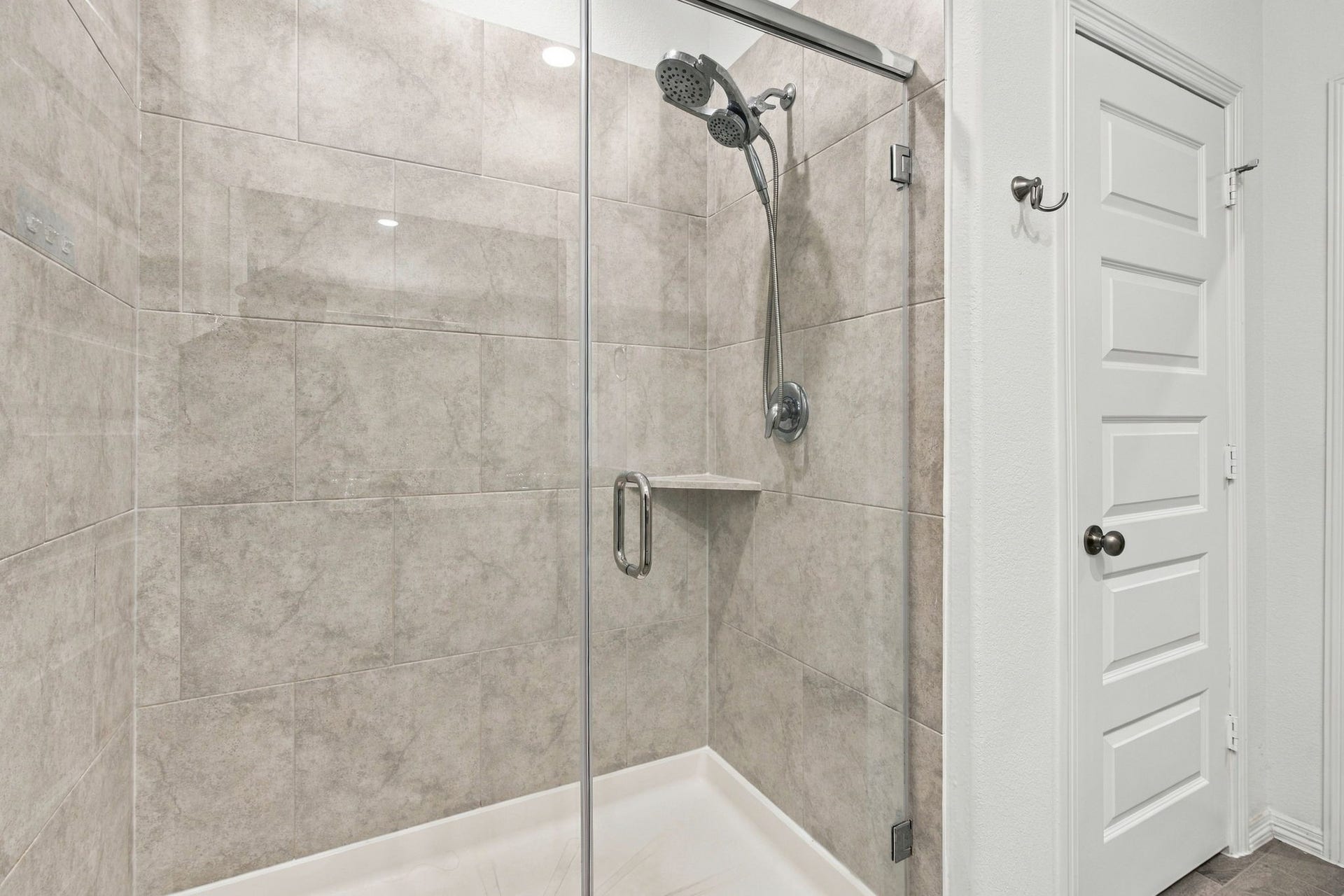 14424 Sunny Bend Way, Conroe, TX 77303 This beautifully designed walk-in shower features elegant, large-format gray tile extending from floor to ceiling, creating a sleek and modern appearance. A frameless glass enclosure with a chrome handle adds a sophisticated touch while maintaining an open, airy feel.