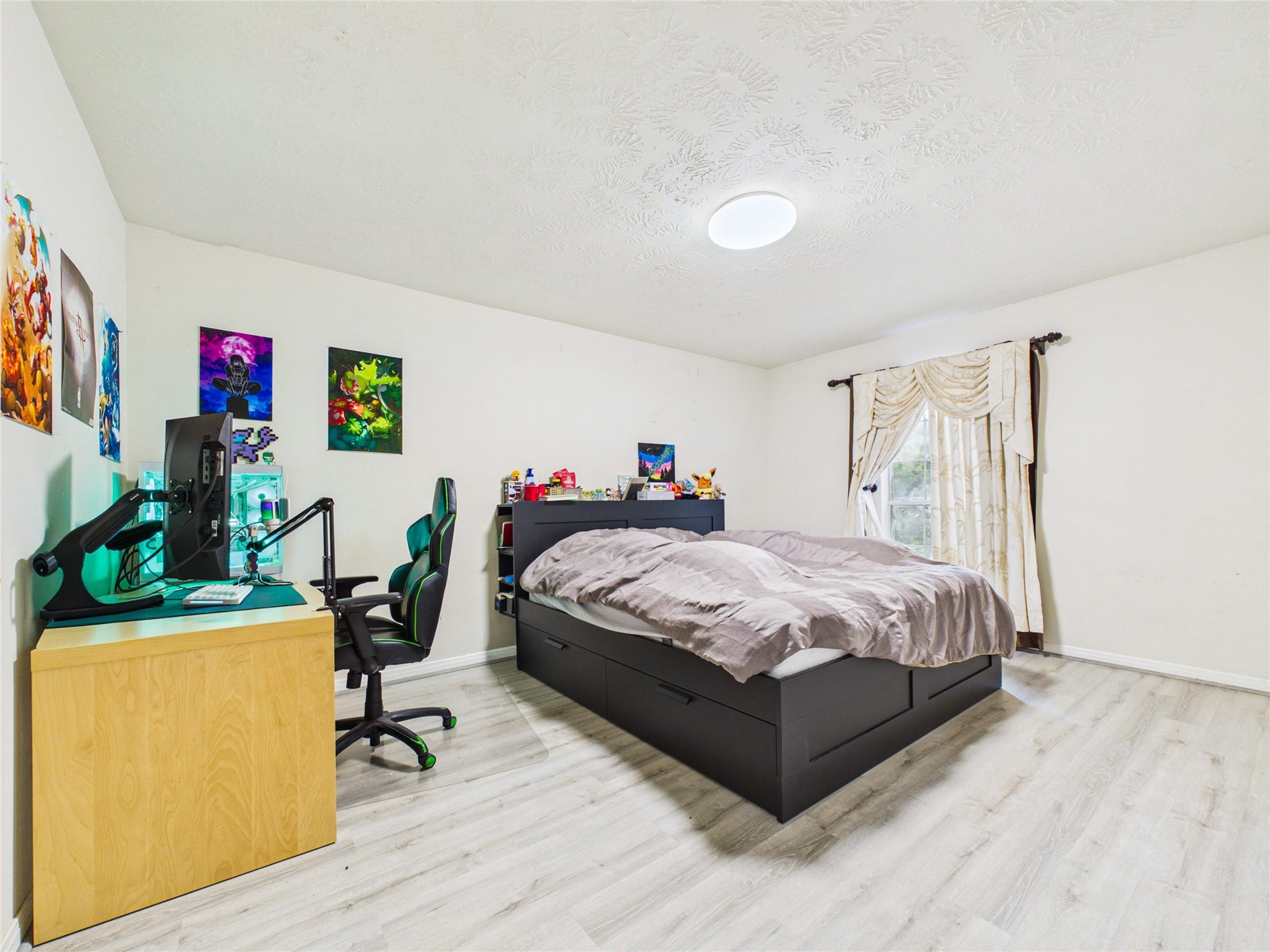 Spacious bedroom with modern wood flooring, featuring a cozy bed with built-in storage, and a functional desk setup perfect for work or gaming.