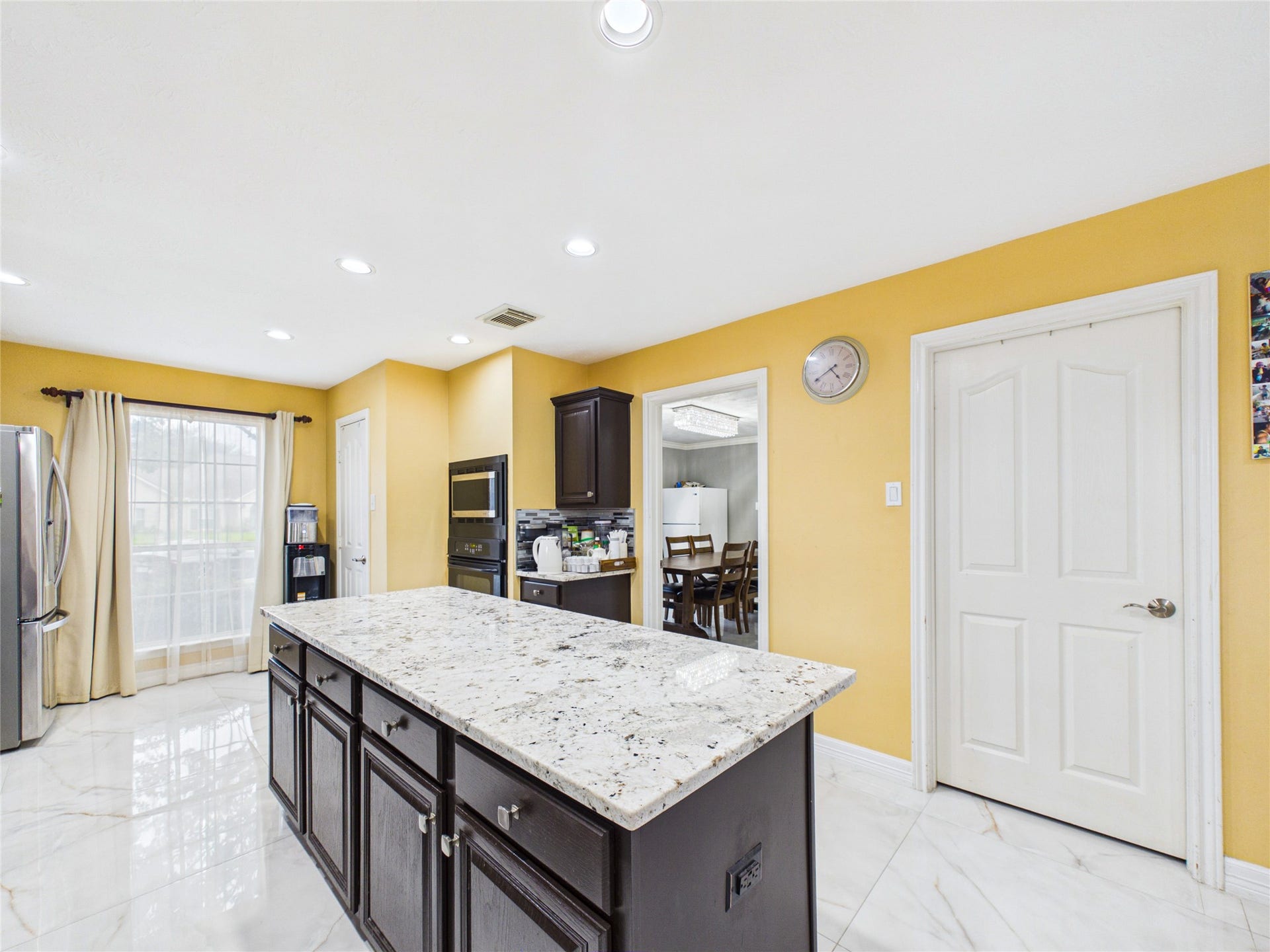 Spacious kitchen with a large granite island, stainless steel appliances, and ample natural light from floor-to-ceiling windows.