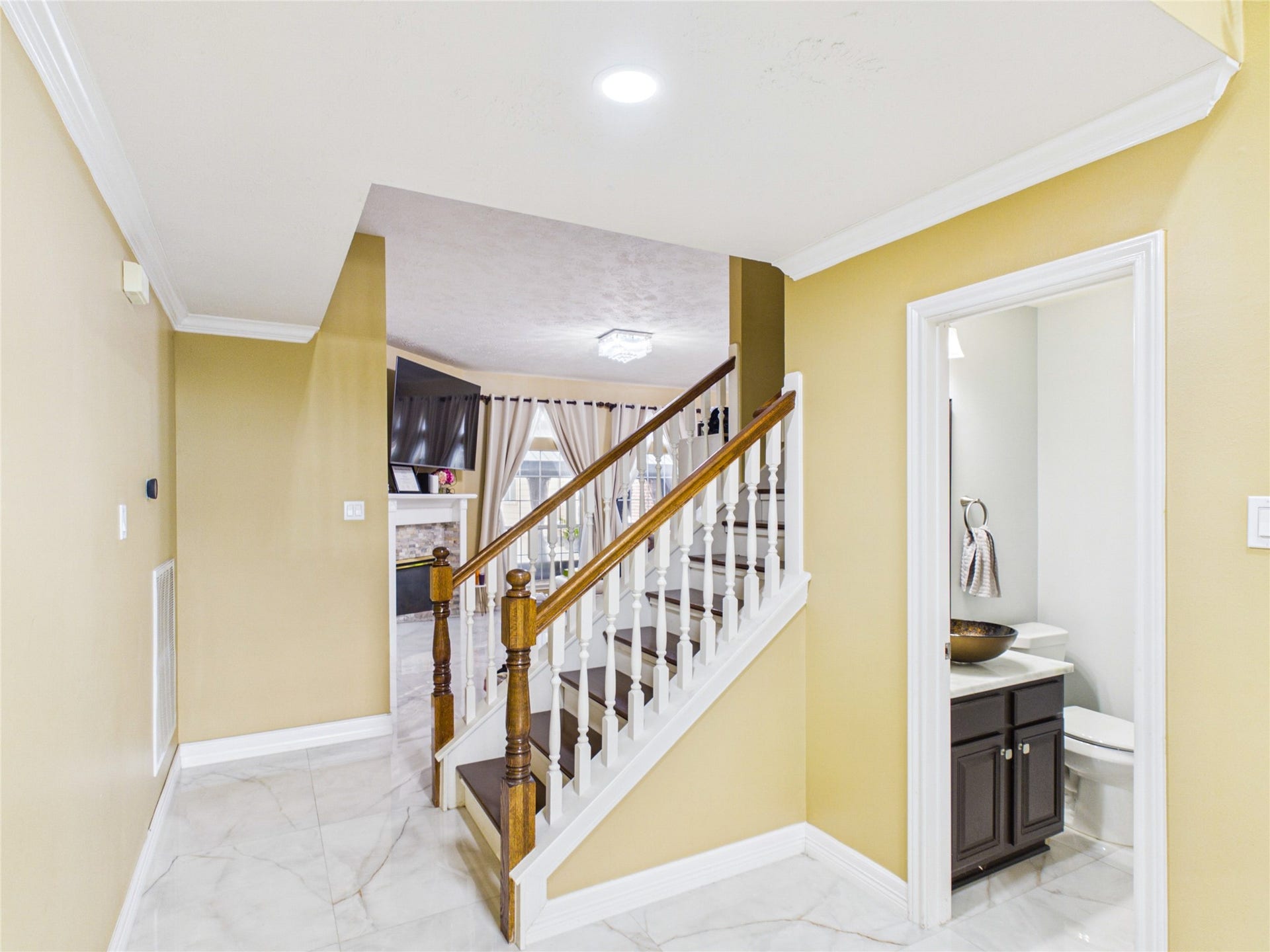 Elegant foyer with glossy tile flooring, a warm-toned staircase, and adjacent powder room, leading to an inviting living area with a cozy fireplace.