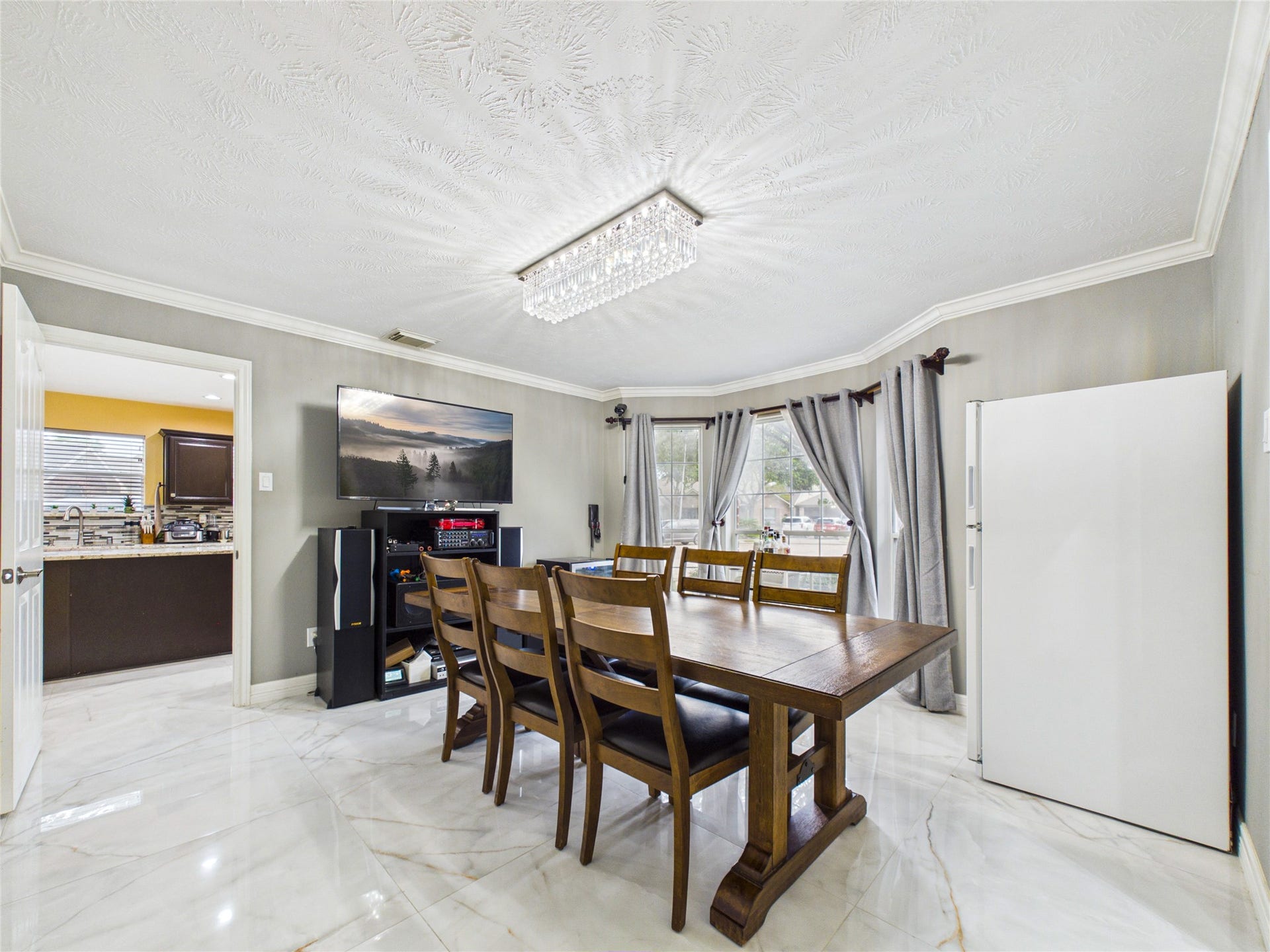 Bright dining area with elegant tile flooring, a modern chandelier, and ample natural light from large windows, seamlessly connecting to the kitchen.