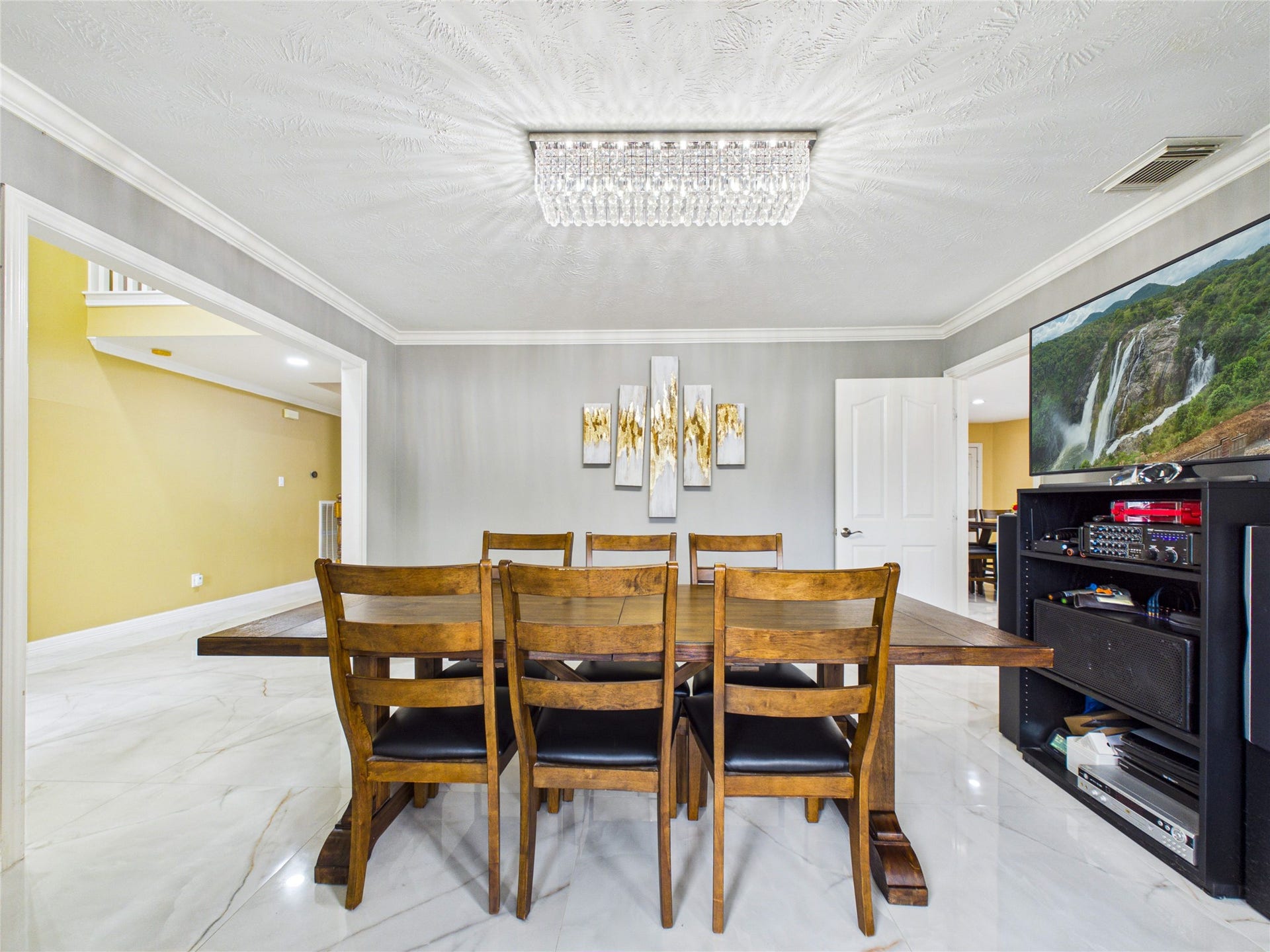 Elegant dining area with a stylish wooden table set, complemented by a modern chandelier and tasteful wall art. The space features sleek marble flooring and a cozy, open layout.
