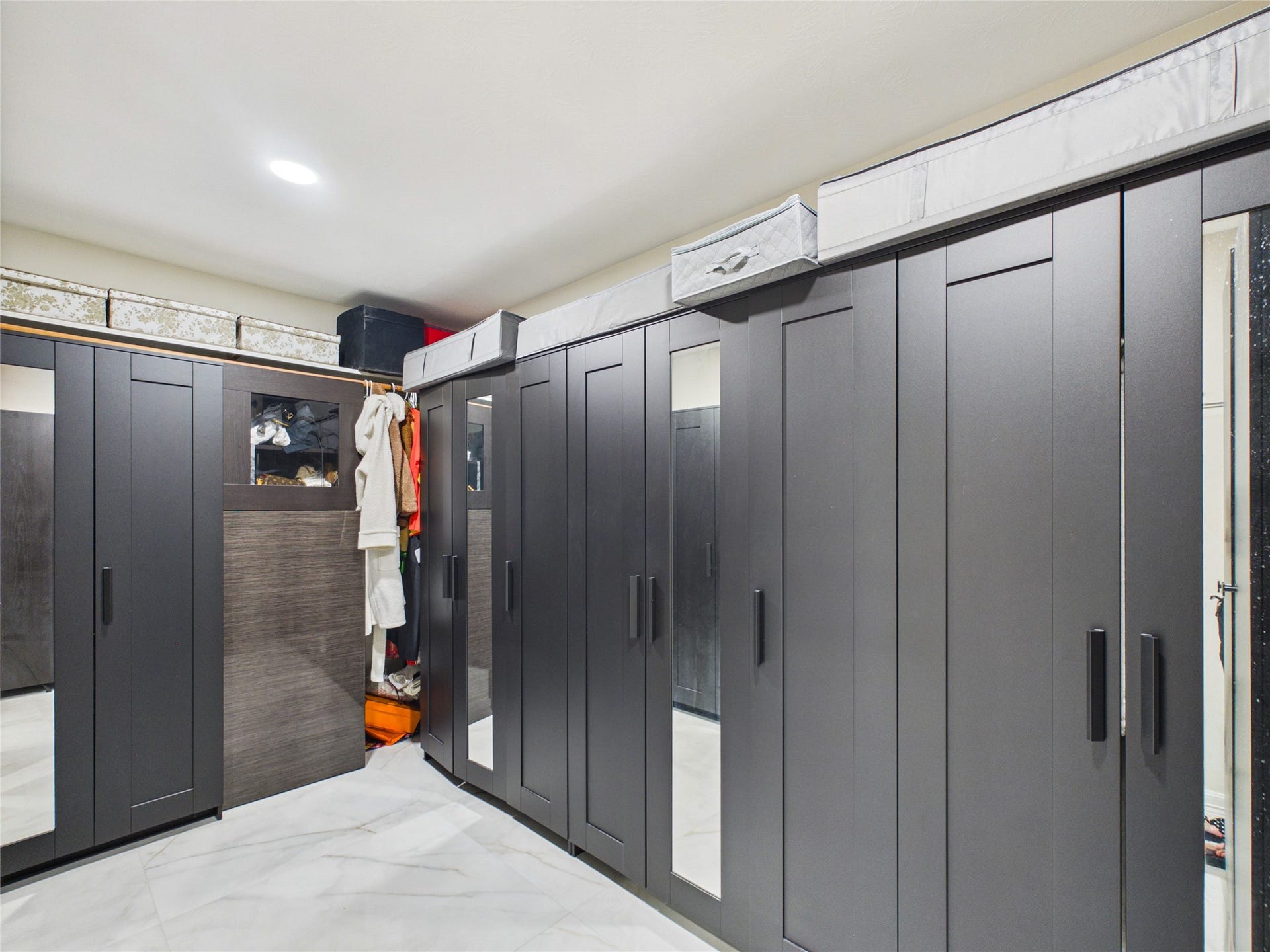 Spacious walk-in closet with sleek, dark cabinetry and ample storage options, featuring built-in mirrors and contemporary design.