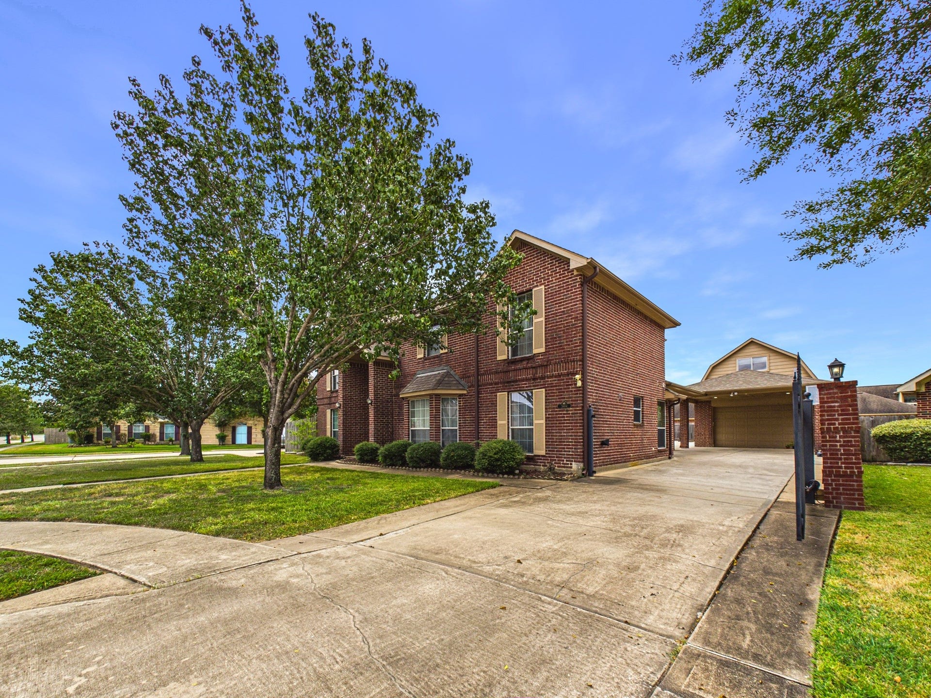 Spacious two-story brick home with a large driveway, mature trees, and a detached garage, offering ample parking and curb appeal.