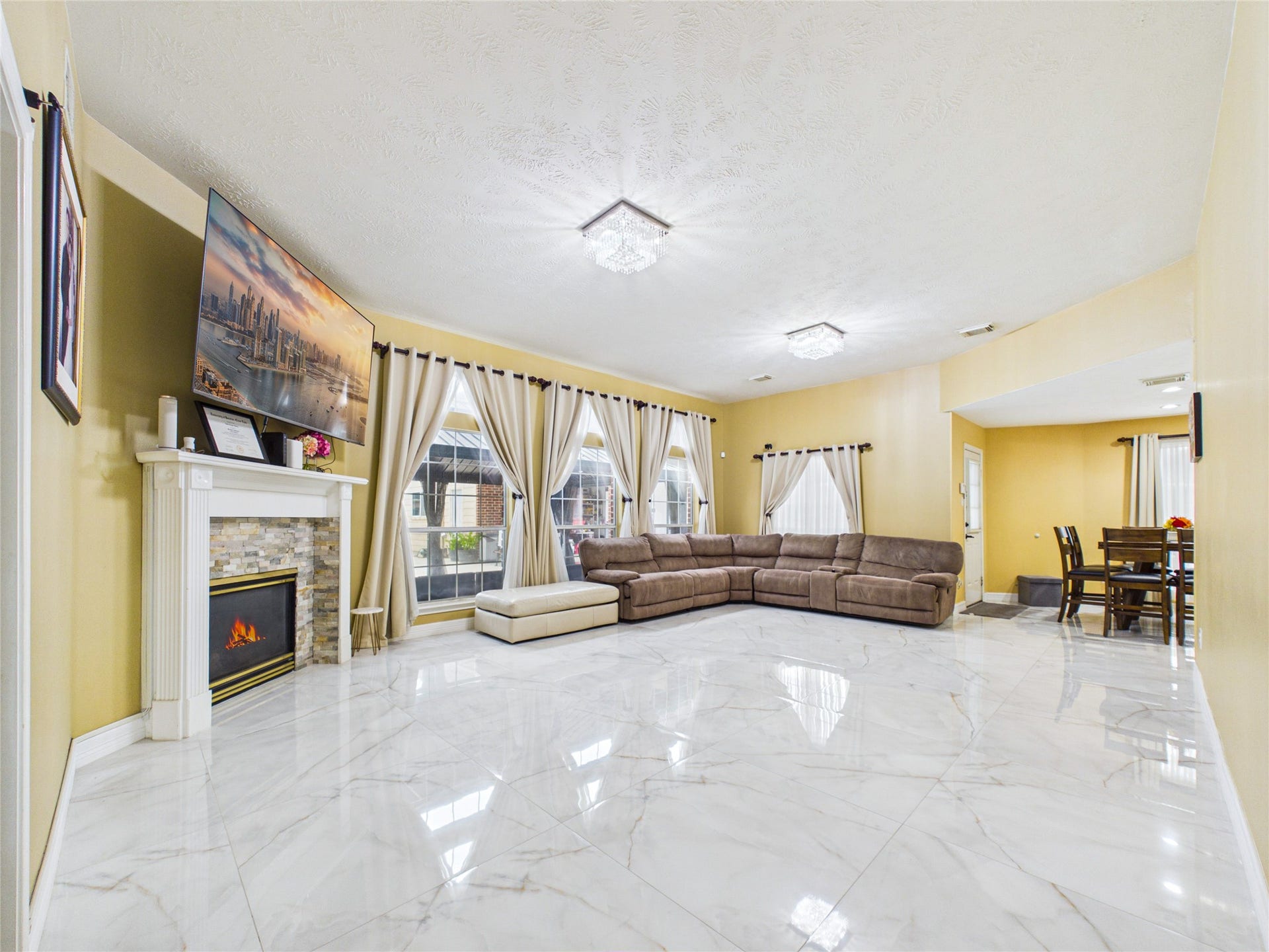 Spacious living area with elegant marble floors, a cozy fireplace, and abundant natural light from large windows, perfect for relaxation and entertaining.