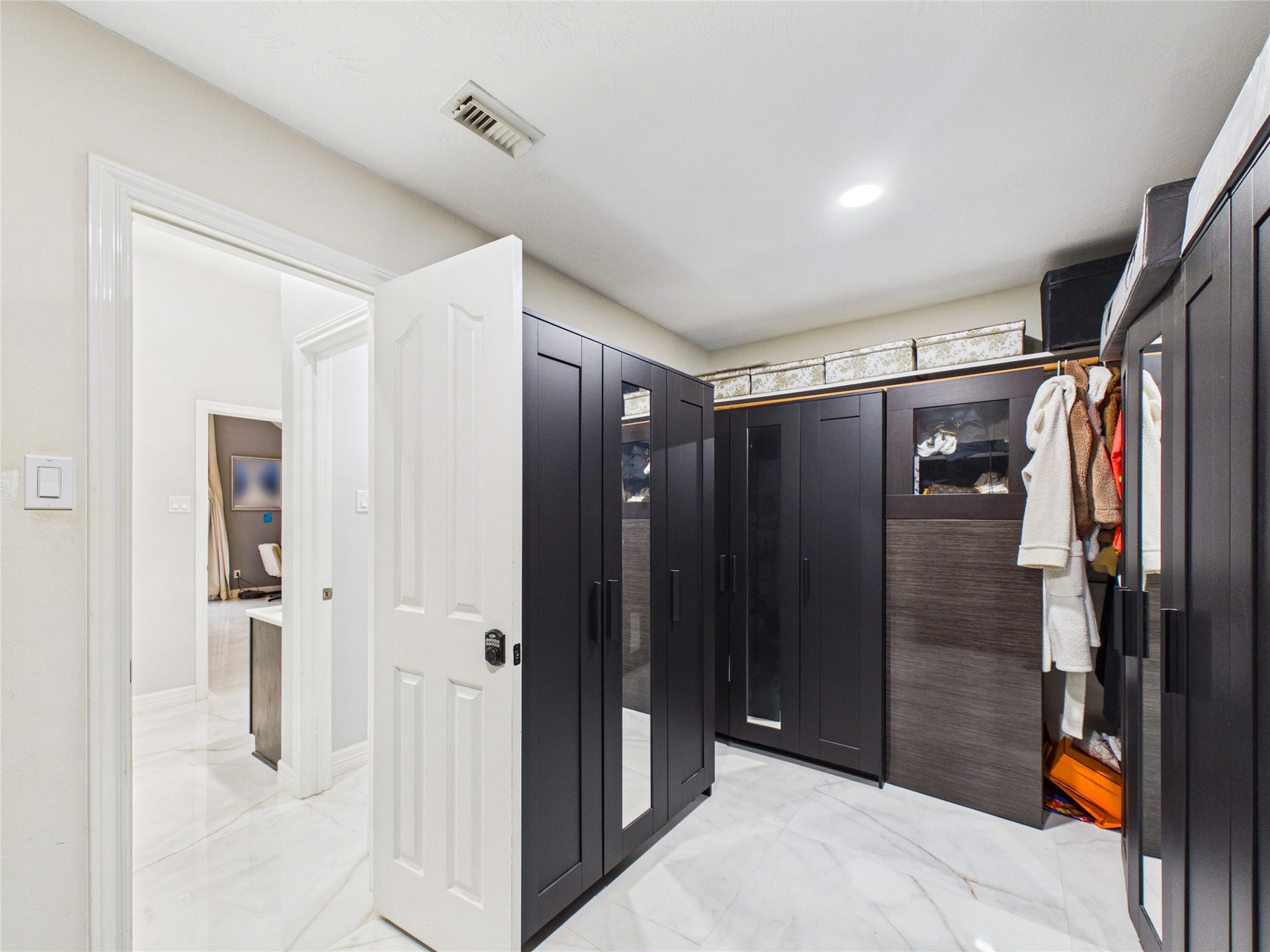 Spacious walk-in closet featuring sleek, dark-wood wardrobes with ample storage and elegant marble flooring.