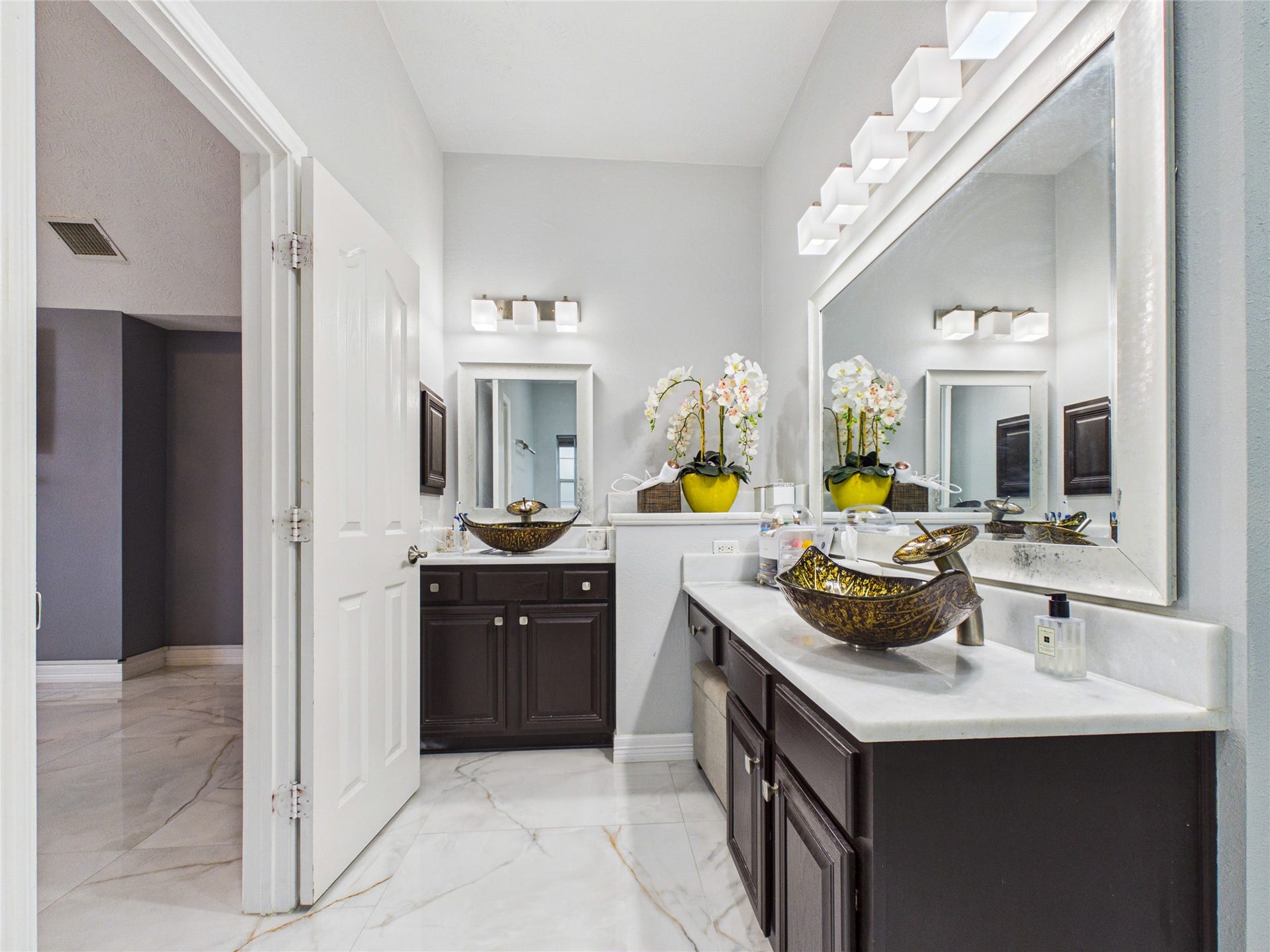 Elegant bathroom featuring dual vanities with vessel sinks, stylish dark wood cabinetry, and modern lighting, complemented by sleek white countertops and marble flooring.