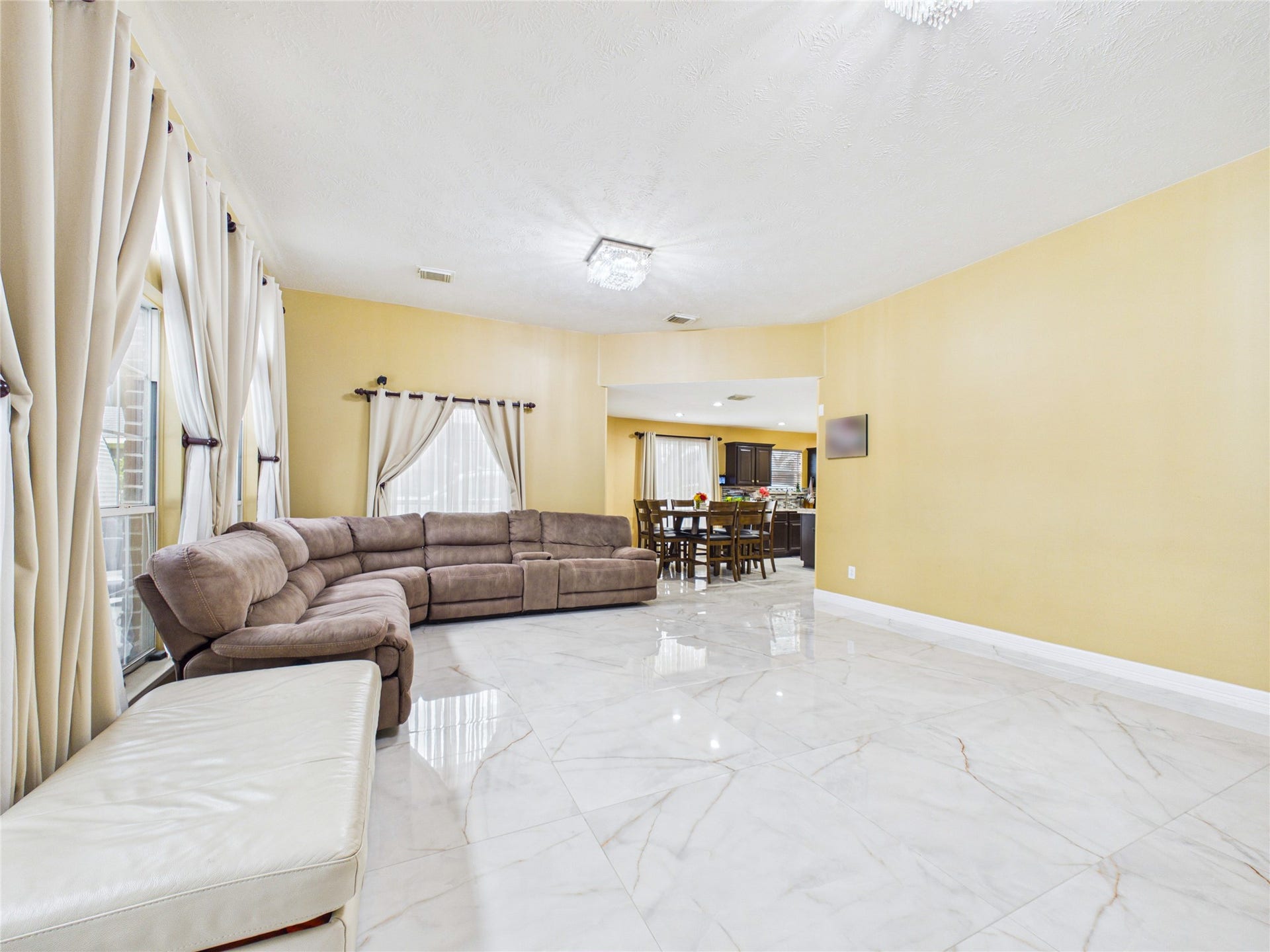 Spacious living area with elegant marble flooring, abundant natural light from large windows, and a cozy sectional sofa.
