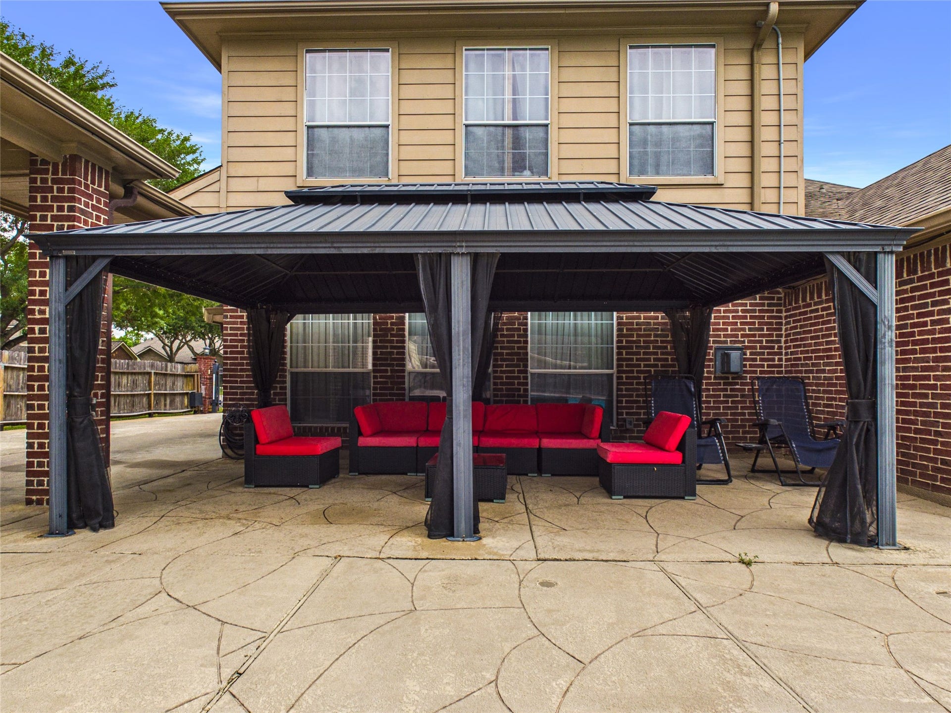 Spacious outdoor patio featuring a stylish gazebo with comfortable red seating, perfect for relaxing and entertaining.