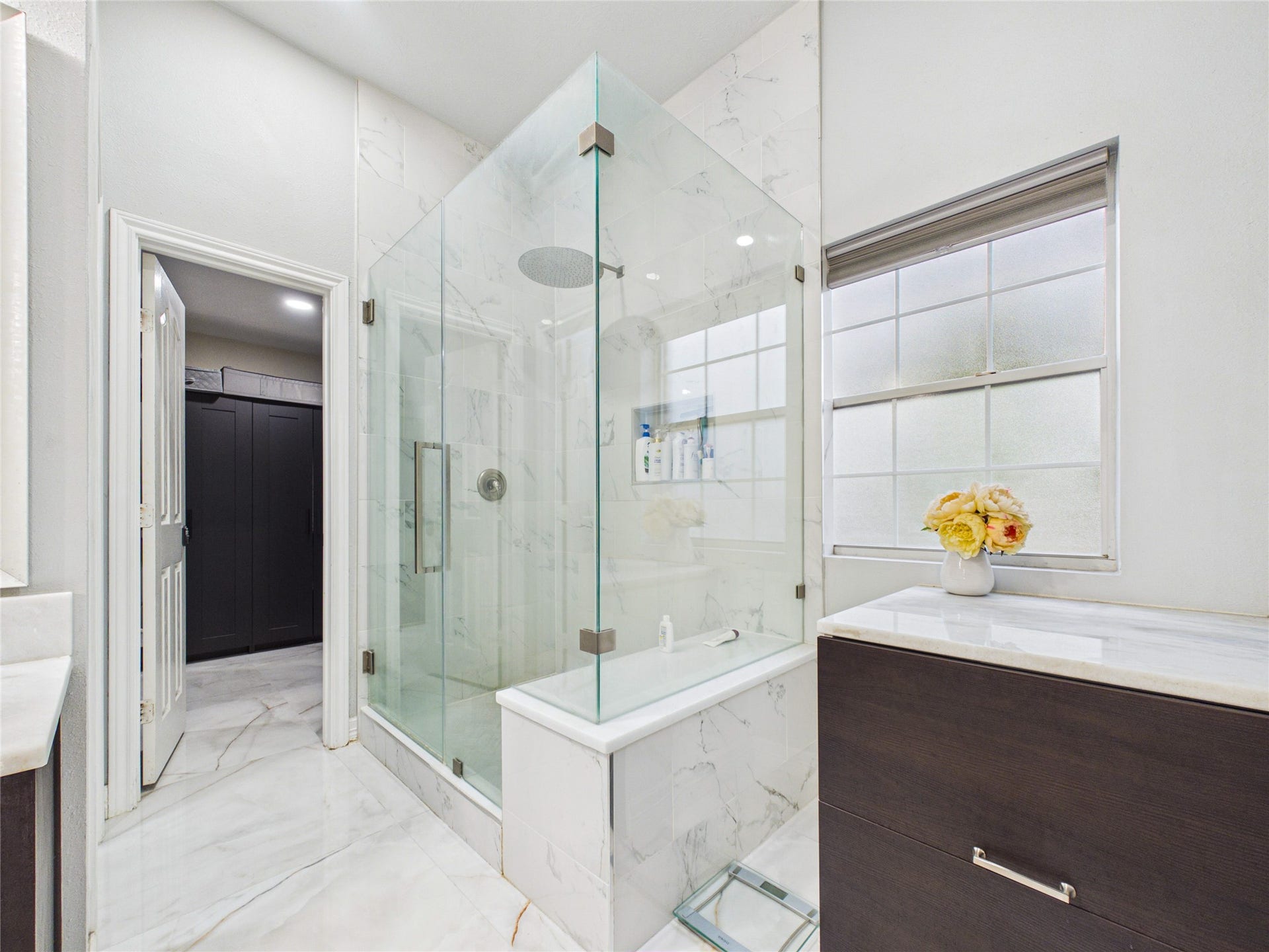 Luxurious bathroom featuring a spacious glass-enclosed shower, elegant marble flooring, and abundant natural light enhancing the modern design.