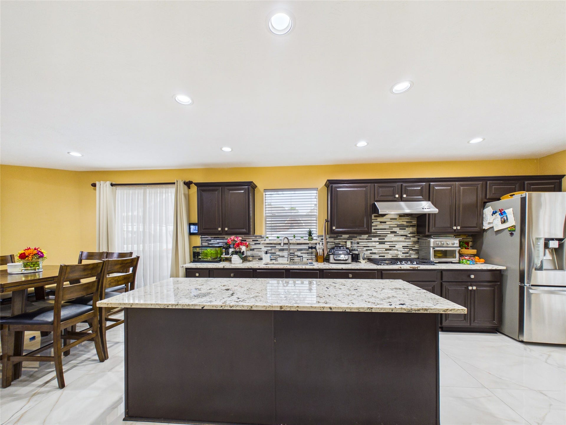 Spacious kitchen with modern dark cabinetry, sleek granite countertops, and stainless steel appliances, complemented by a stylish tile backsplash. A cozy dining area adjoins the kitchen, perfect for entertaining.