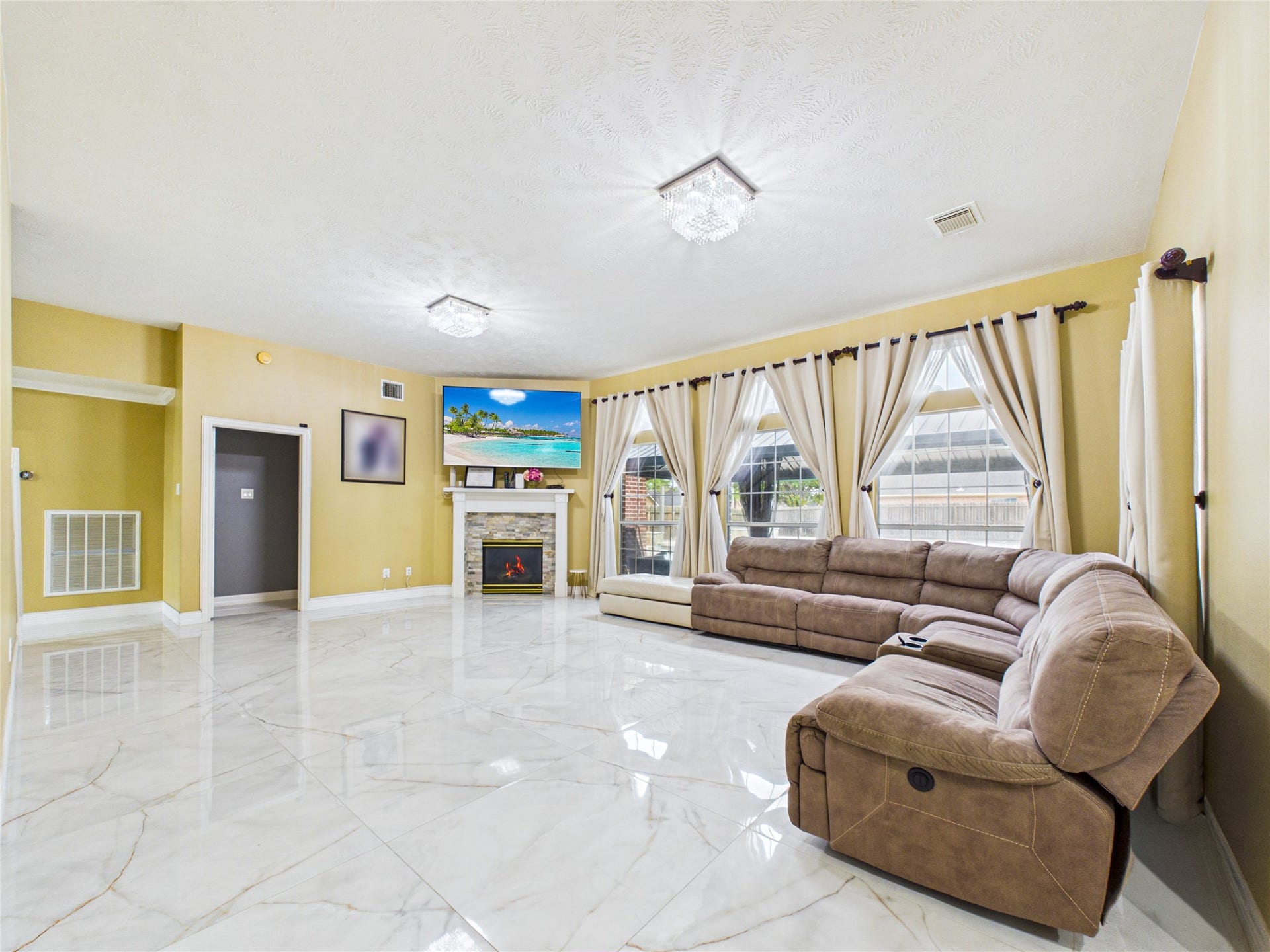Spacious living room with glossy tile flooring, large windows for abundant natural light, and a cozy fireplace beneath a mounted TV.