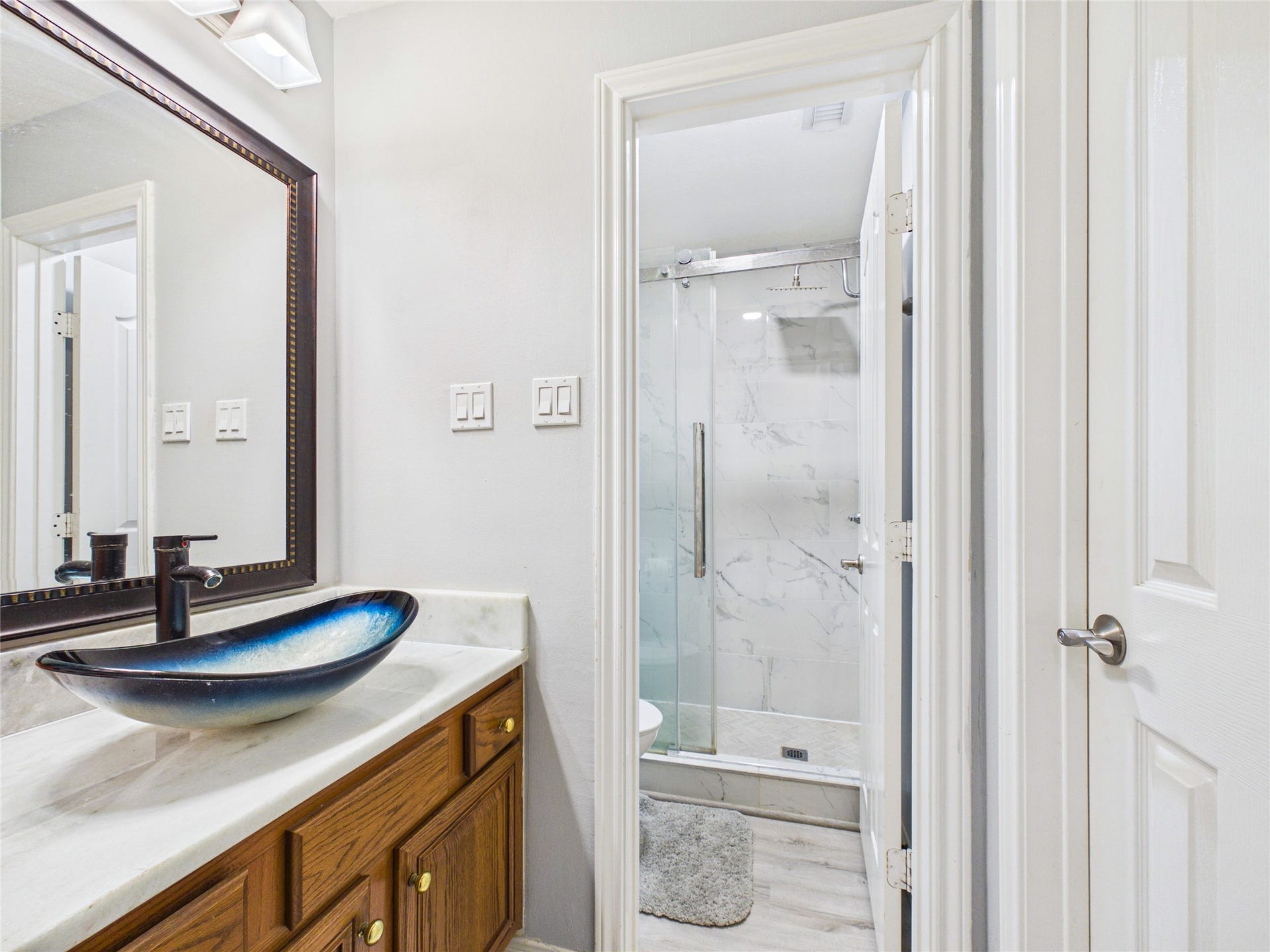 Chic bathroom featuring a modern vessel sink and elegant marble shower, complemented by warm wood cabinetry and sleek fixtures.