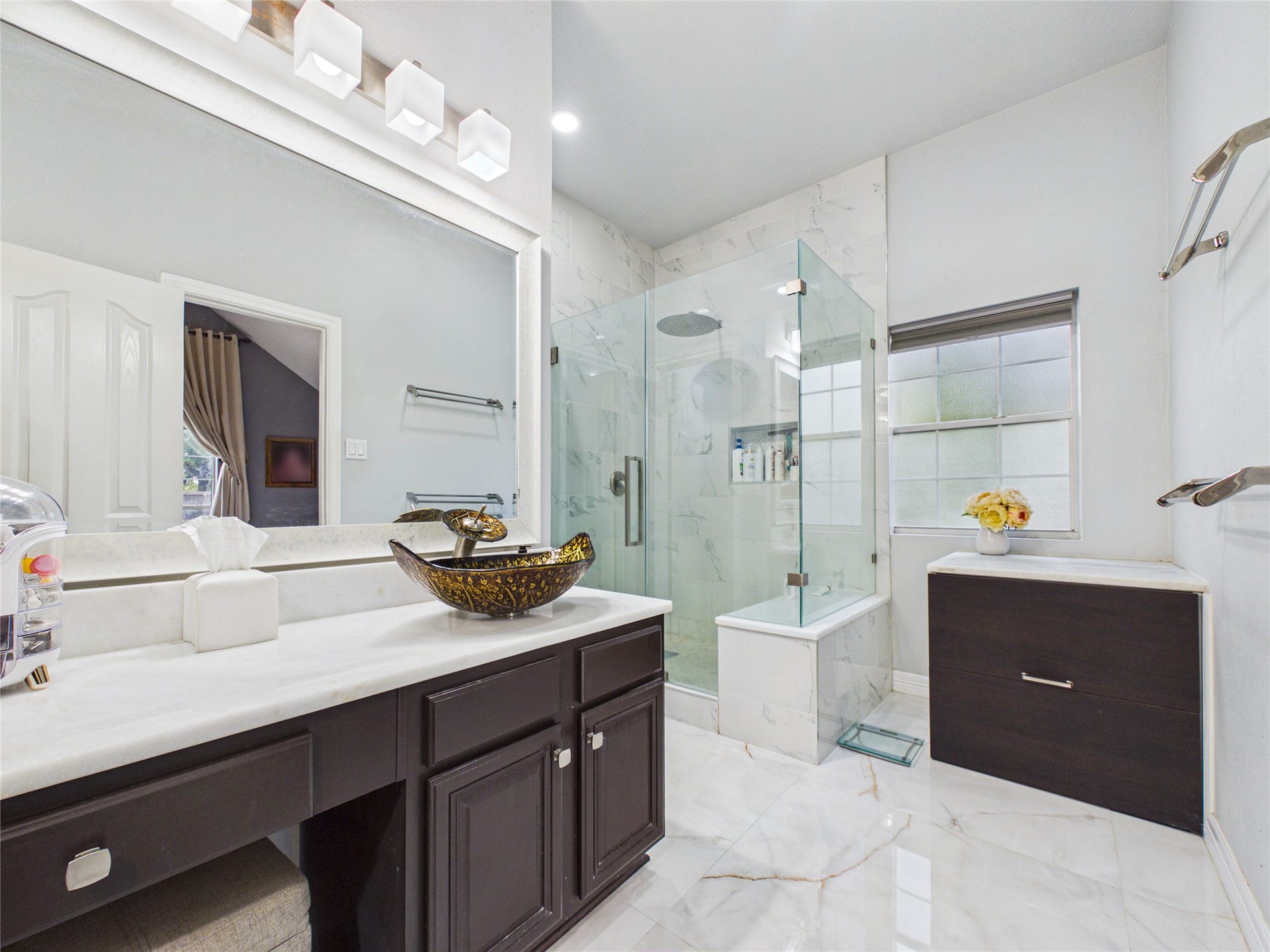 Elegant bathroom featuring a luxurious glass-enclosed shower, modern vessel sink, and sleek cabinetry, all enhanced by marble flooring and soft natural light.