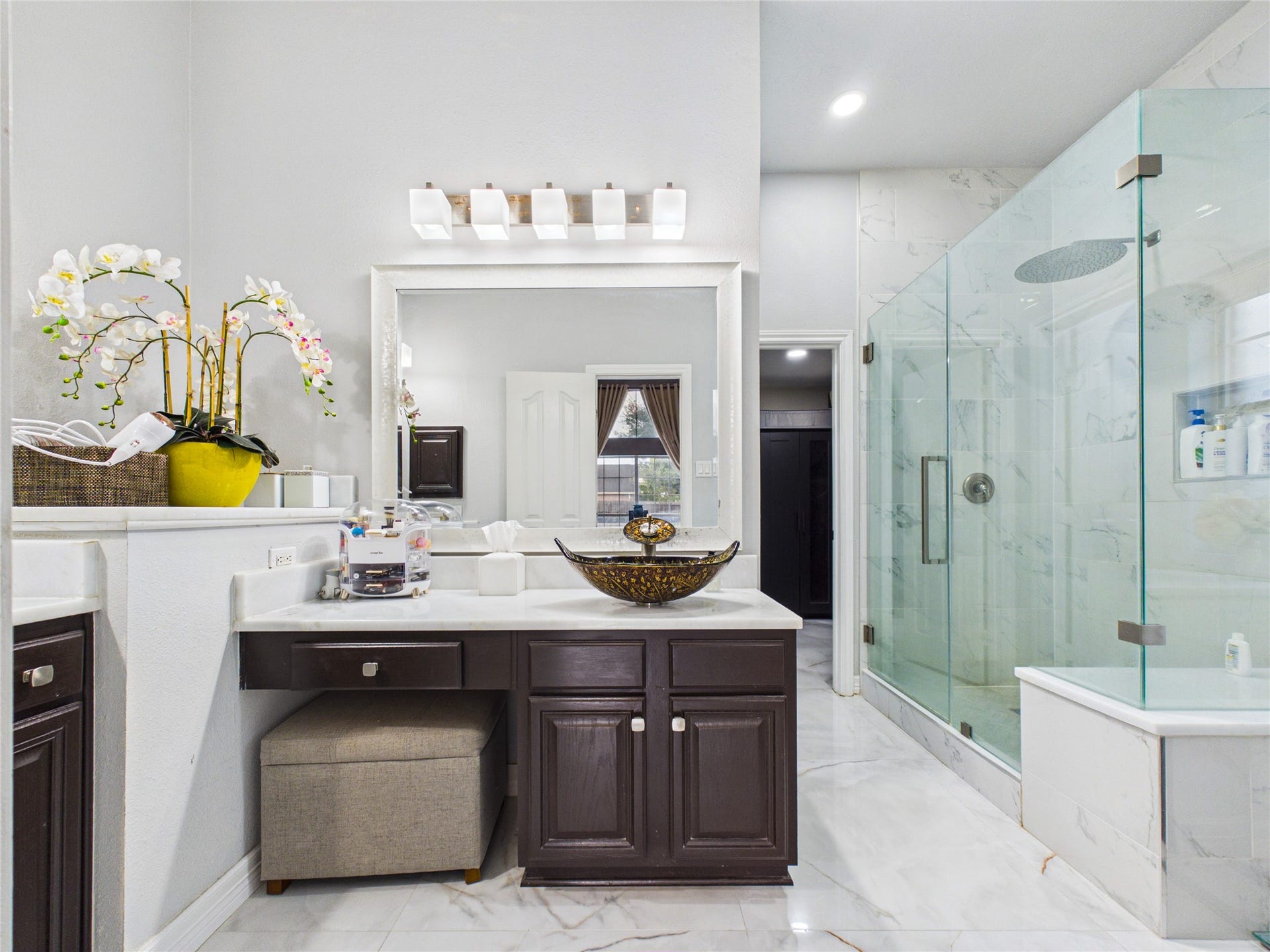 Elegant bathroom featuring a modern glass-enclosed shower, stylish vessel sink, and sleek dark cabinetry, all complemented by bright lighting and a touch of greenery.