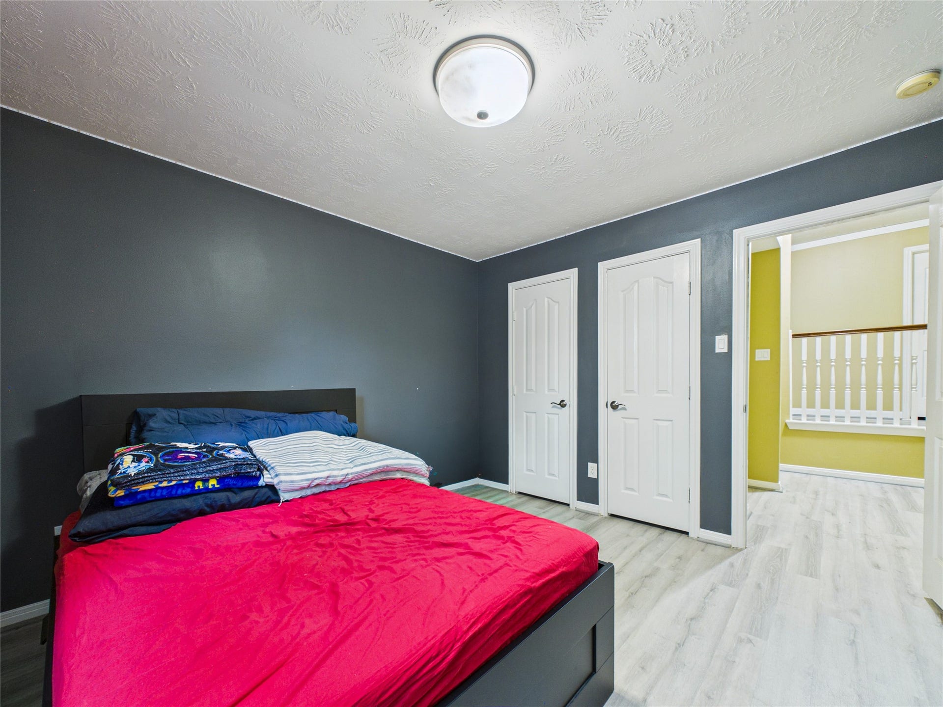 Cozy bedroom featuring sleek dark walls, light wood flooring, and convenient dual closets, offering a modern and functional space.