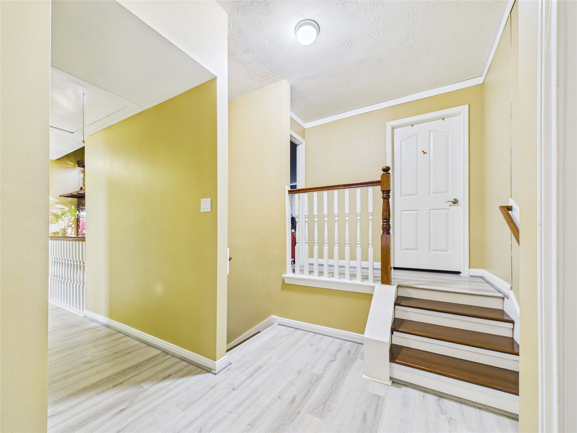 Bright and inviting hallway with elegant wood flooring, a charming staircase, and crisp white accents.