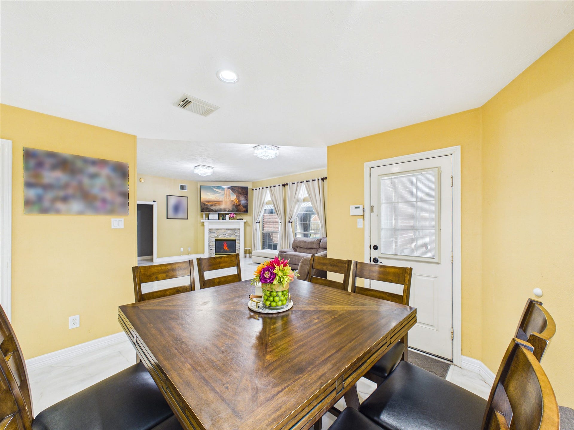 Bright and inviting dining area with a stylish wooden table, leading to a cozy living room with a charming fireplace and large windows for natural light.
