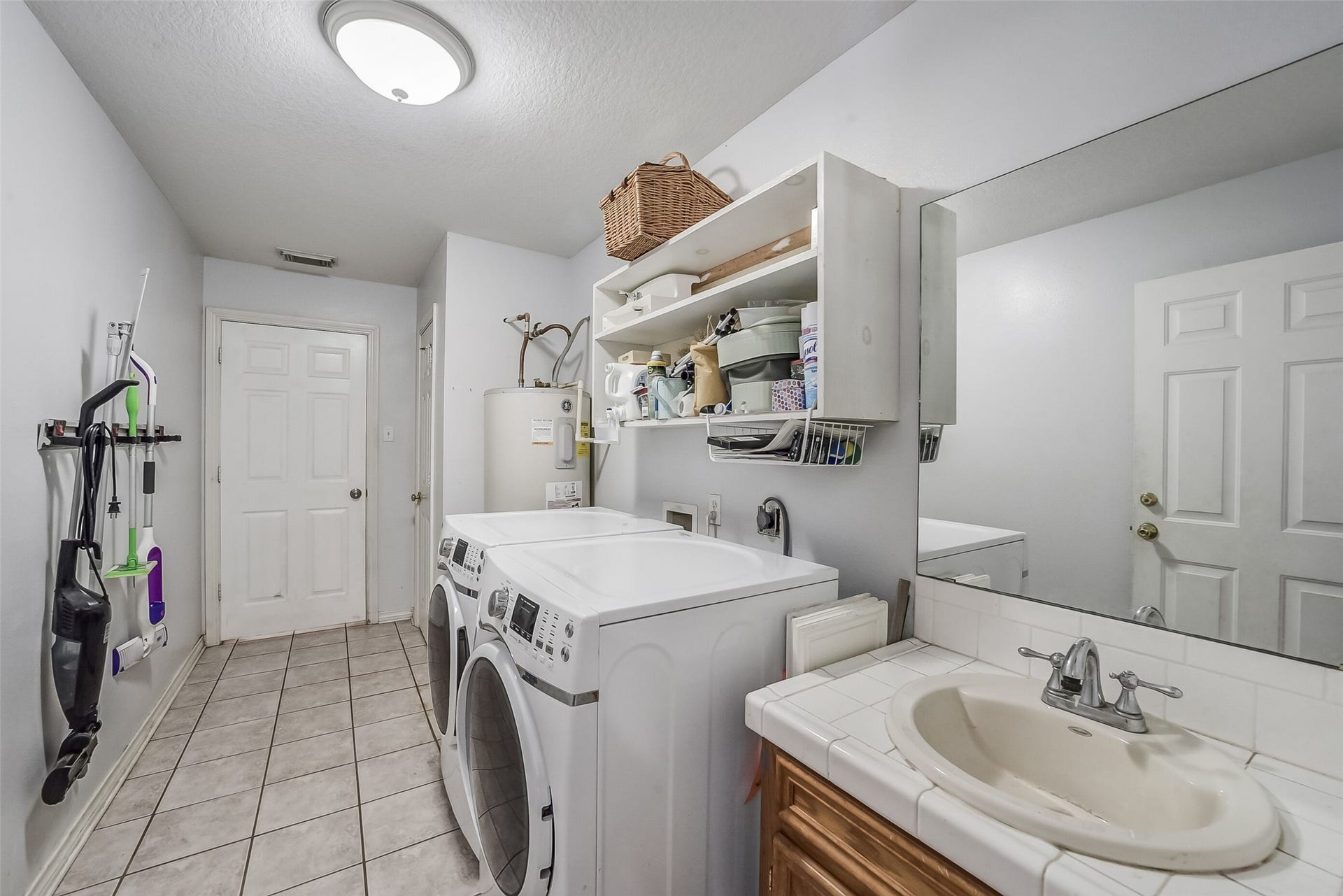 22911 Keith Drive, New Caney, TX 77357 This functional laundry room features tile flooring, overhead shelving for convenient storage, and space for a full-size washer and dryer. A sink with a tiled countertop and lower cabinetry provides added convenience for everyday tasks.