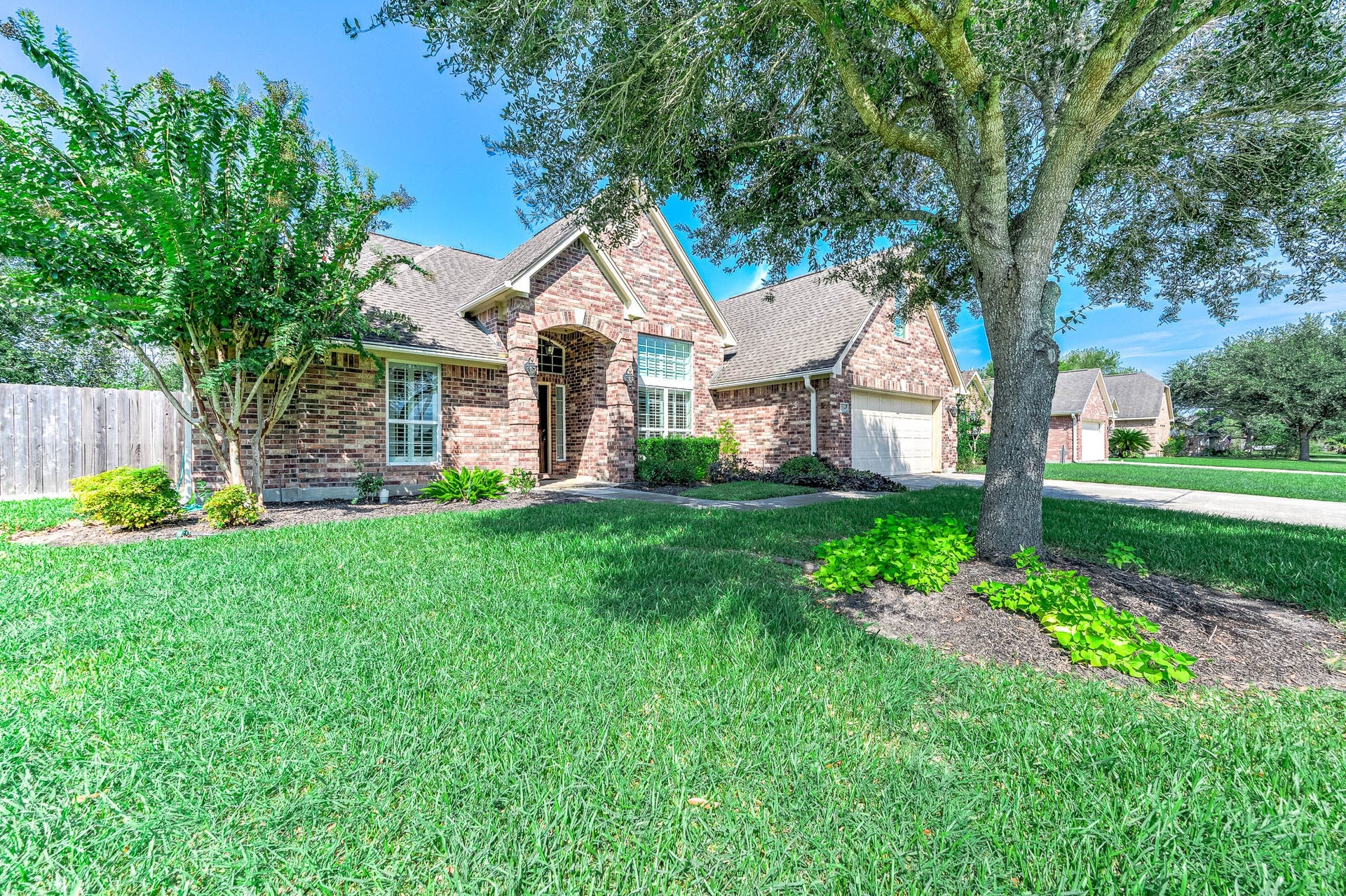 A charming brick home with a mature tree offering cool shade, enhancing the inviting curb appeal.
