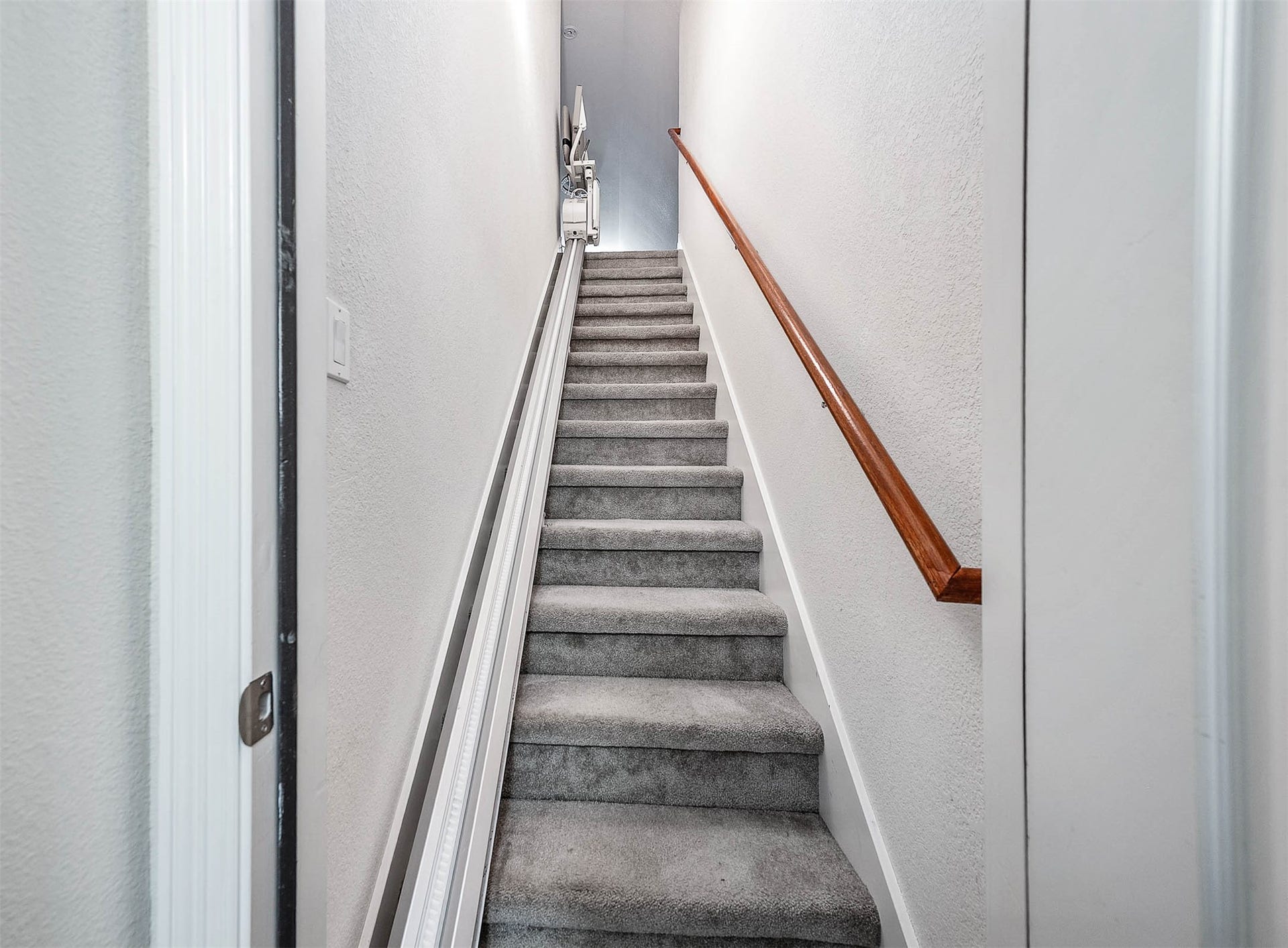 Carpeted staircase with a wooden handrail leads to the upper level, offering a cozy and secure ascent.