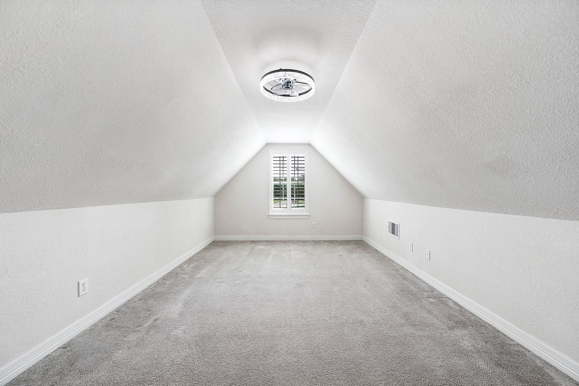 Bright and airy attic space featuring a unique vaulted ceiling, plush carpet, and a central window that invites natural light for a cozy retreat or creative workspace.