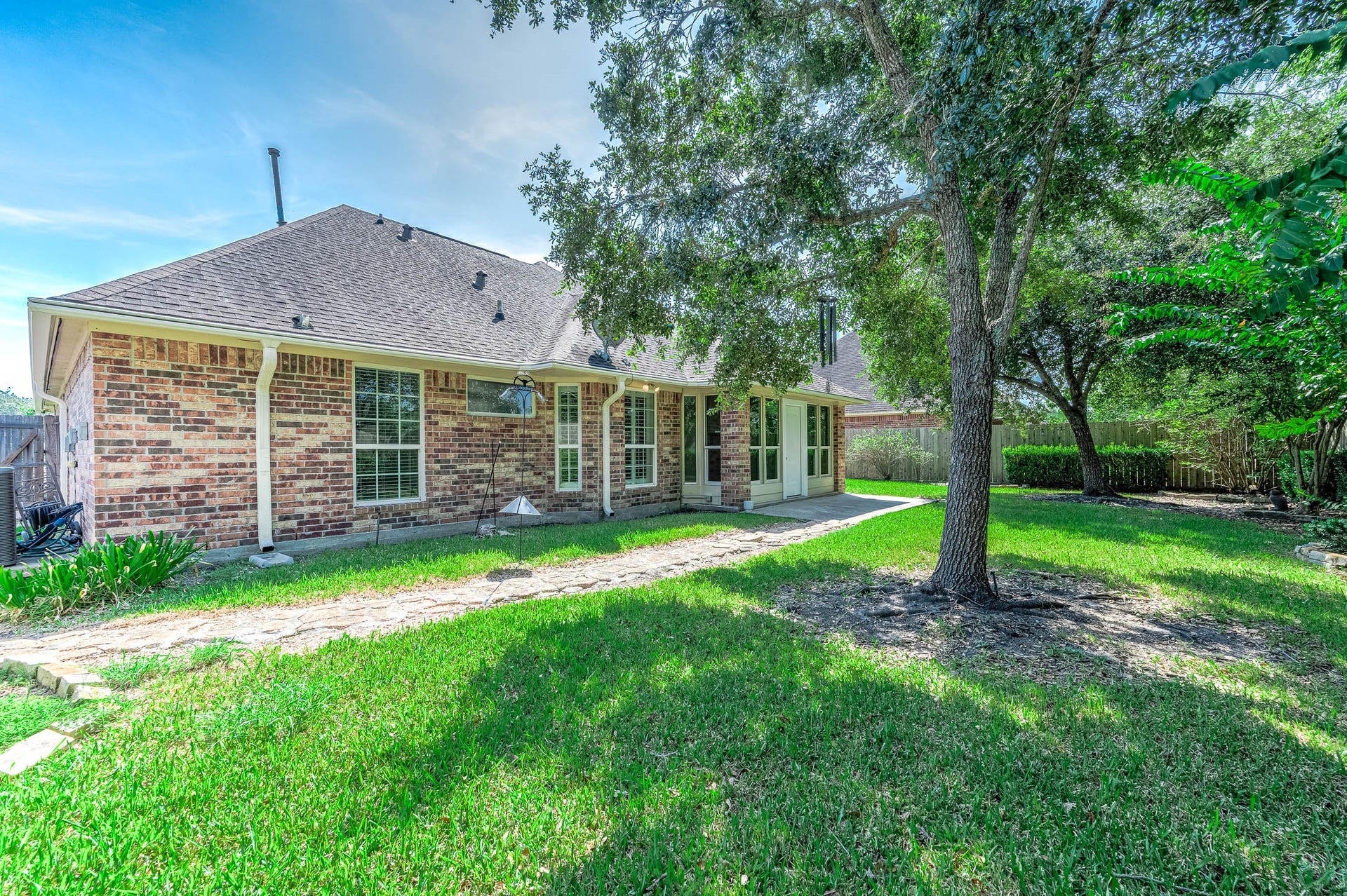 Charming brick home with a spacious backyard, featuring a lovely patio and mature trees providing ample shade.
