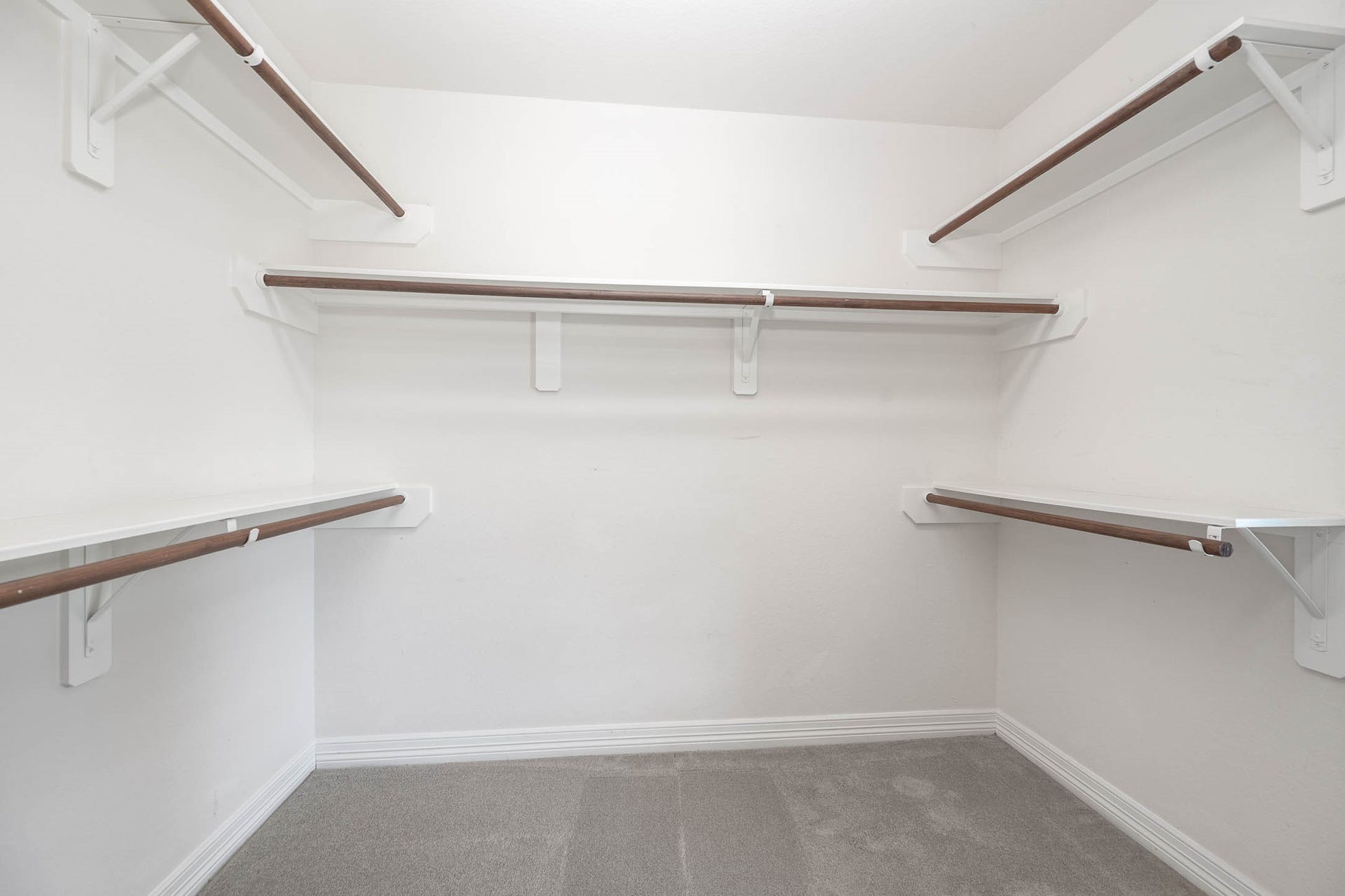 Spacious walk-in closet with multiple wooden hanging rods and ample shelving, perfect for organizing your wardrobe.