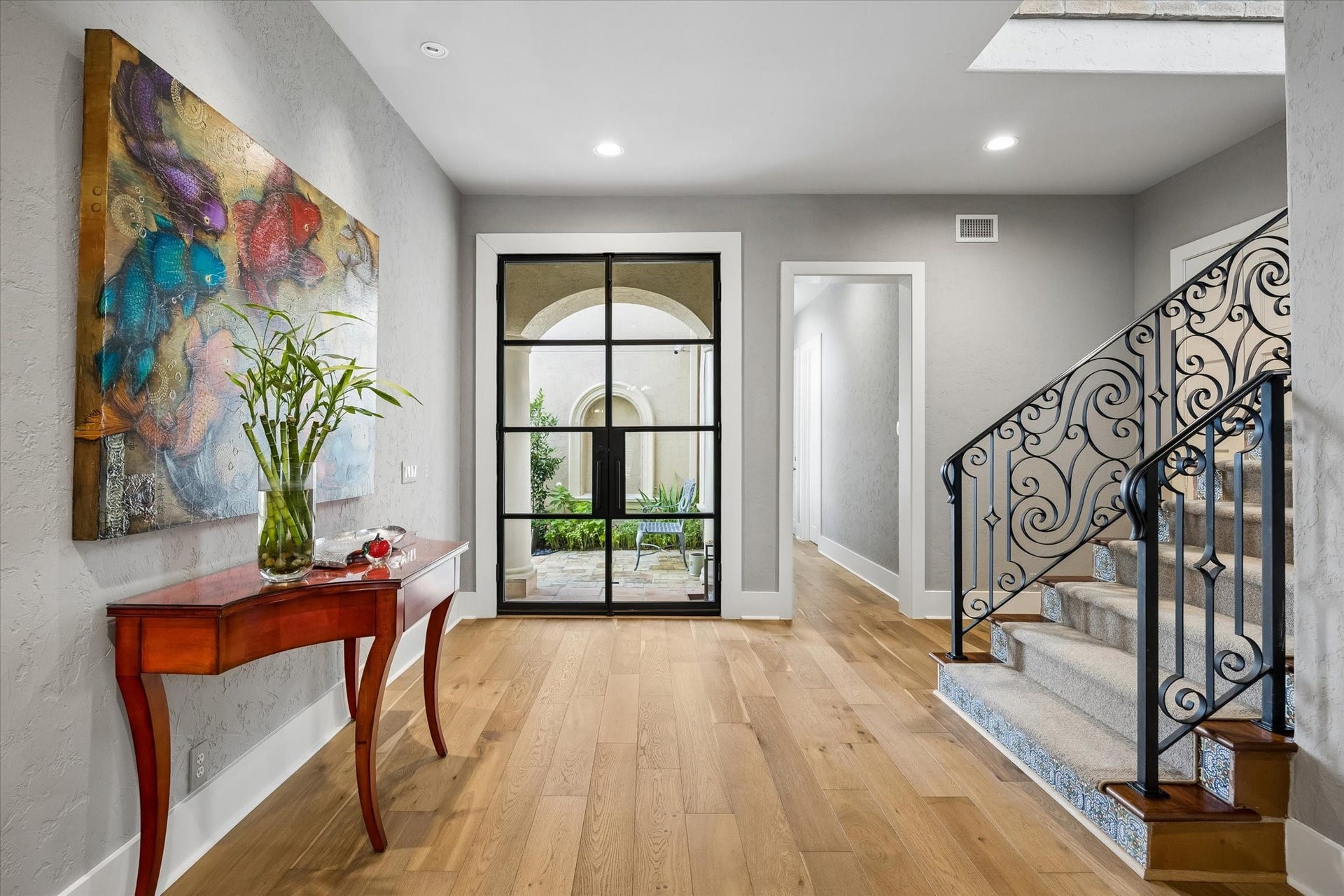 Wide, grand foyer with glass and steel double doors, hardwood floors and staircase with custom runner.