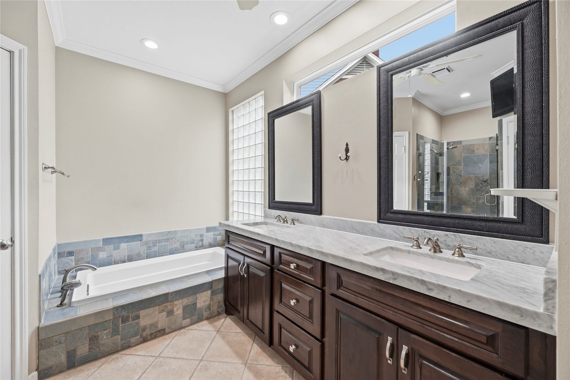 The primary bathroom featuring a double vanity with updated countertops  and a spacious soaking tub with a separate shower.