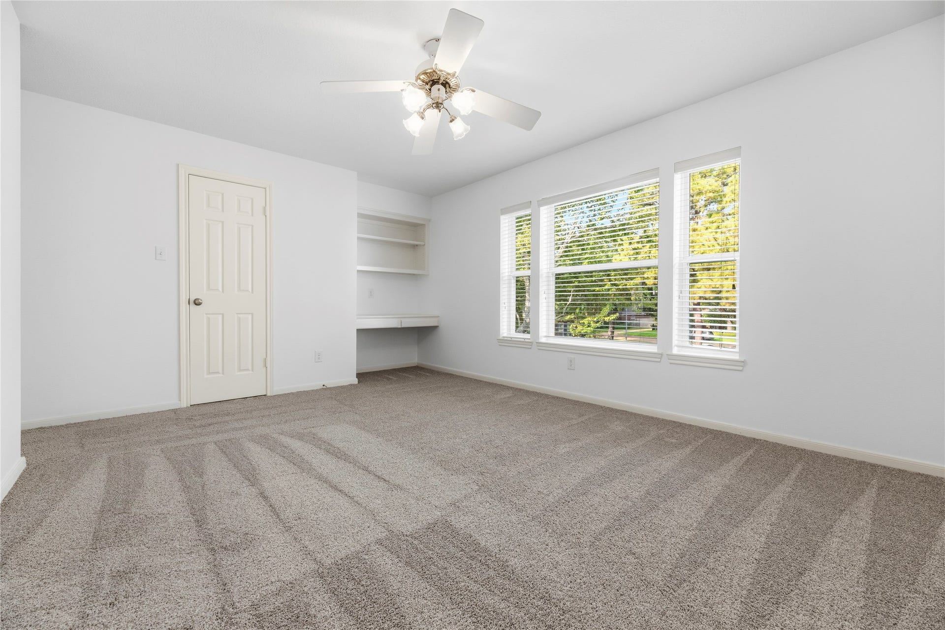 Bright secondary bedroom with plush carpeting (upgraded pad and carpet replaced in 2022). A built-in desk and shelving add functionality to the space.
