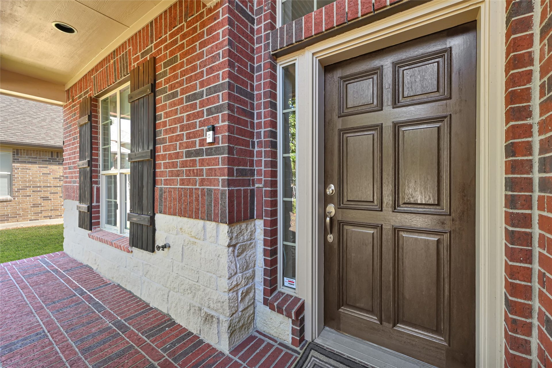 Charming brick exterior with a rich wooden front door and elegant window shutters, offering a warm and inviting entrance.