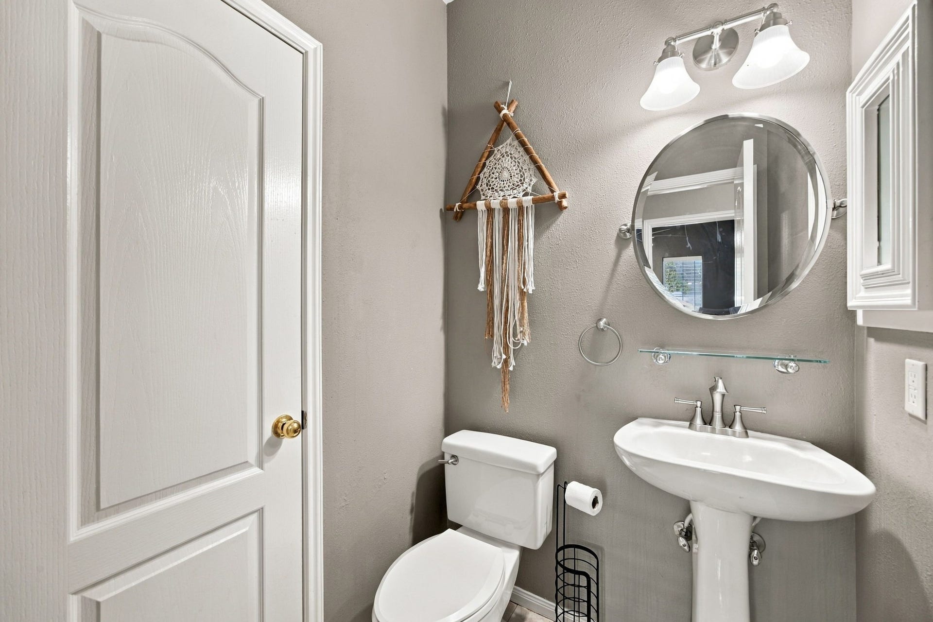 2417 La Rochelle Court, Seabrook, TX 77586 Charming bathroom with a pedestal sink, round mirror, and modern lighting. Decor includes a stylish wall hanging, creating a cozy and inviting atmosphere.