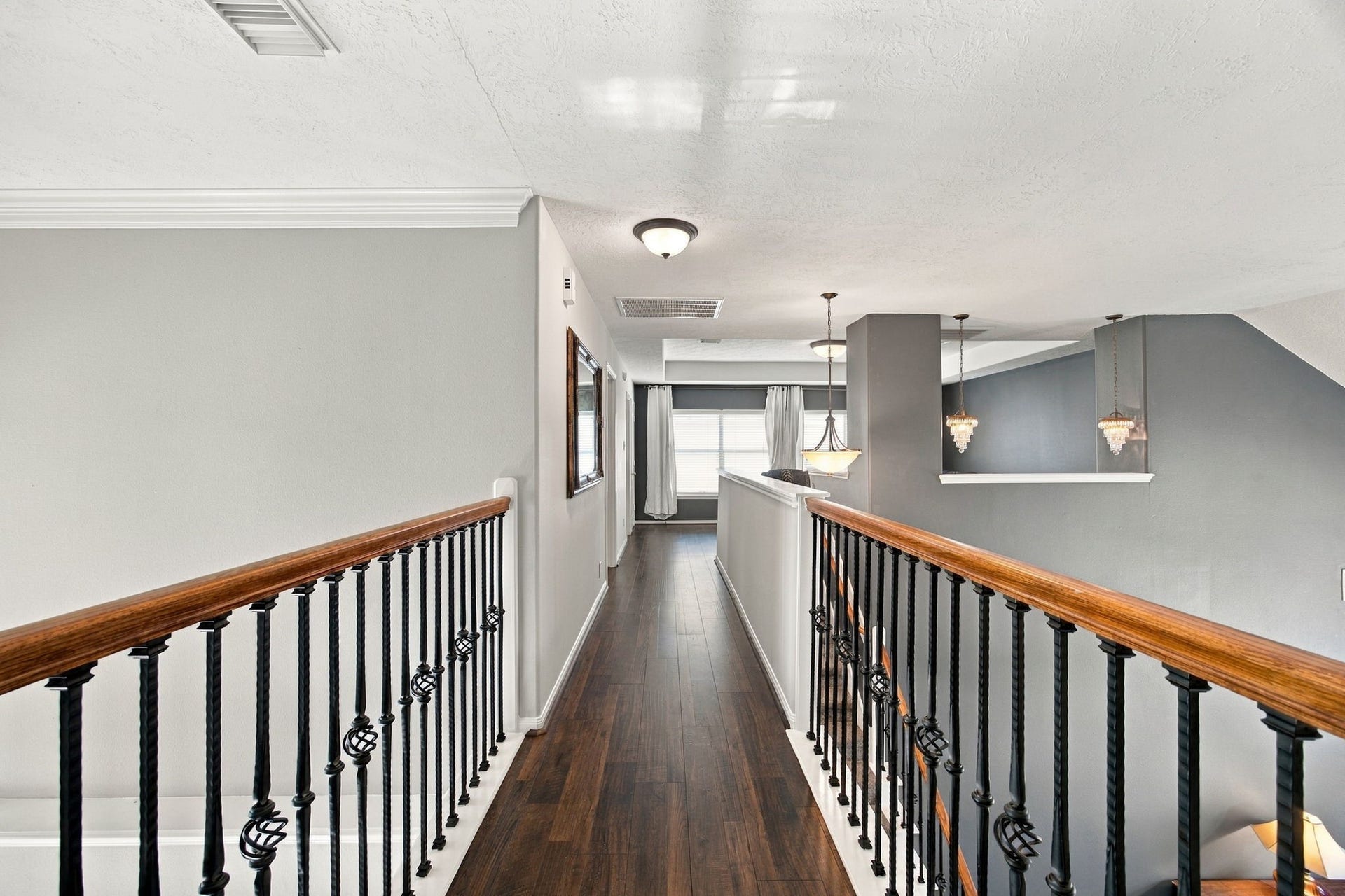 2417 La Rochelle Court, Seabrook, TX 77586 Elegant upstairs hallway with rich wood flooring and stylish wrought-iron railing, leading to bright, inviting rooms.