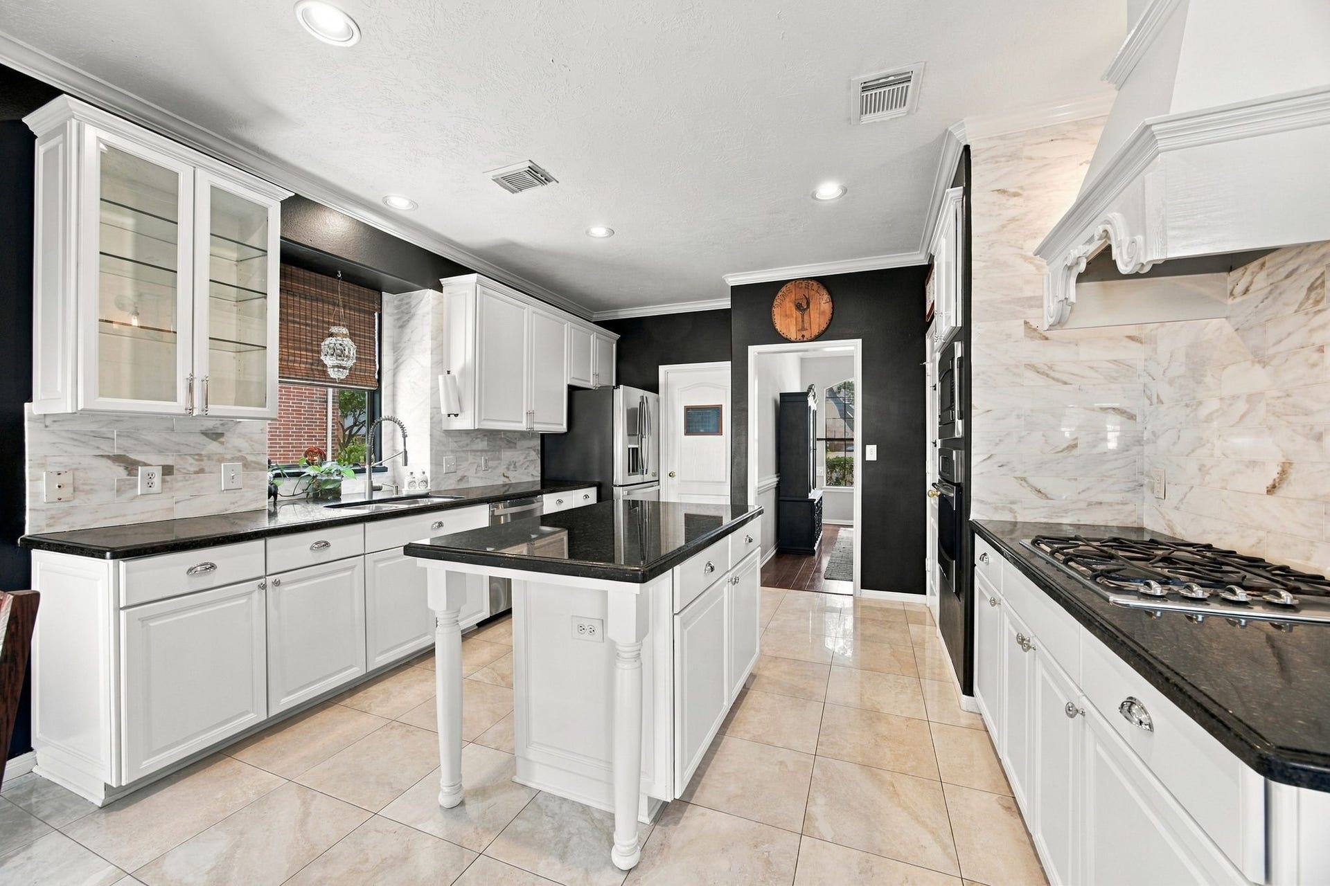 2417 La Rochelle Court, Seabrook, TX 77586 Elegant kitchen featuring sleek black granite countertops, white cabinetry, and a central island, complemented by stainless steel appliances and a stylish tile backsplash.