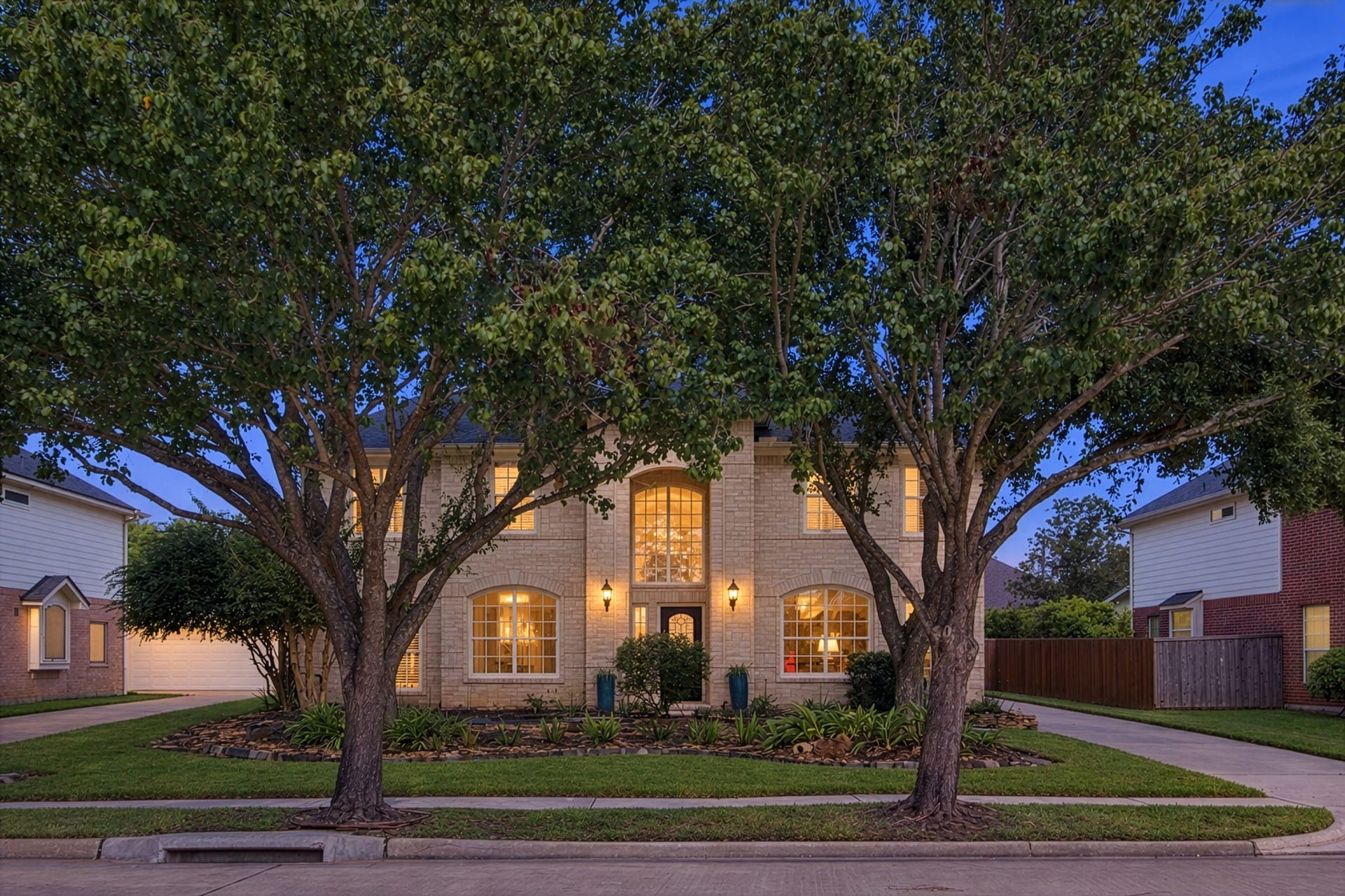 2417 La Rochelle Court, Seabrook, TX 77586 Stately two-story brick home framed by mature trees, featuring large arched windows and a welcoming front entrance.