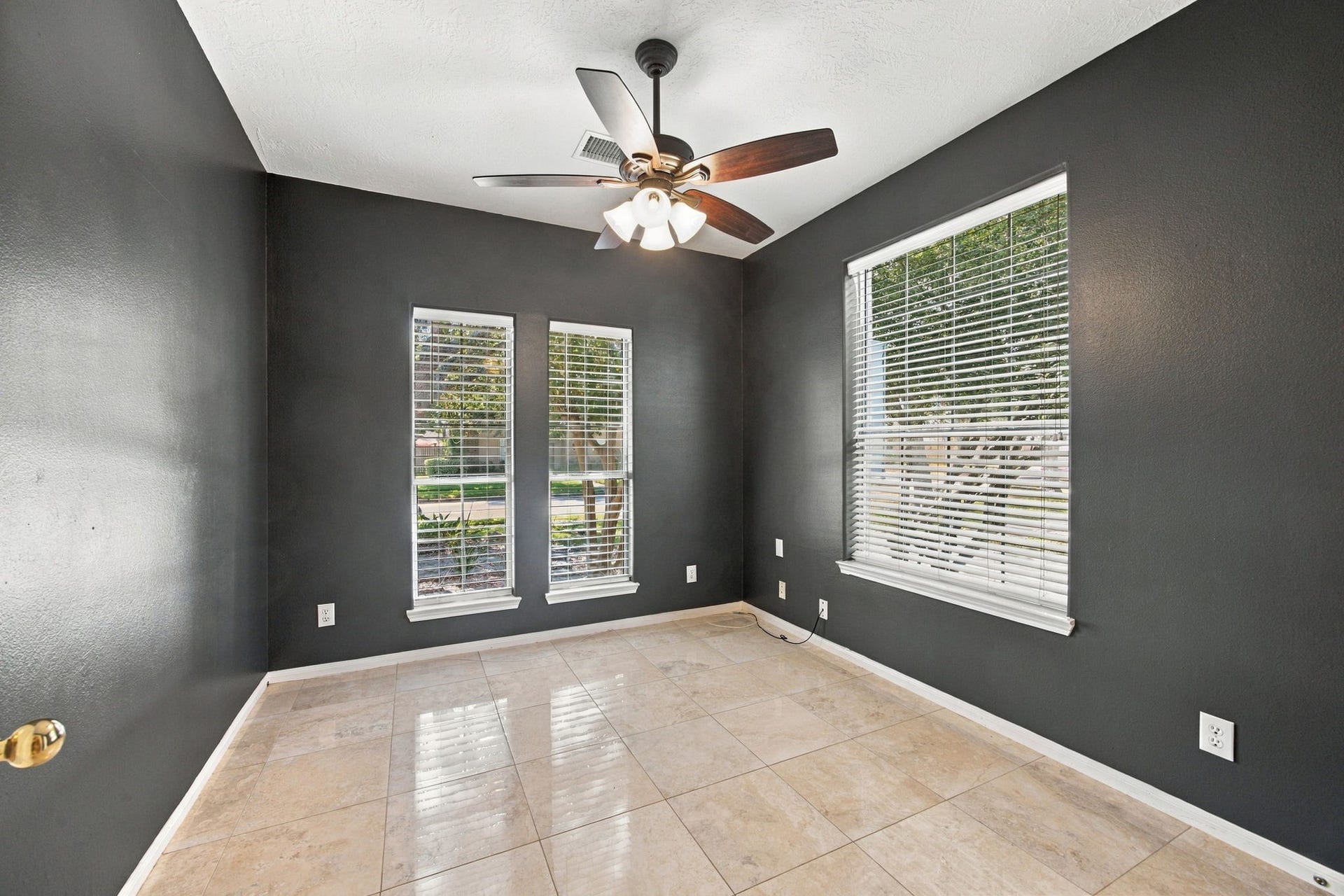 2417 La Rochelle Court, Seabrook, TX 77586 A cozy room with sleek dark walls and large windows providing abundant natural light, complemented by elegant tile flooring and a modern ceiling fan.