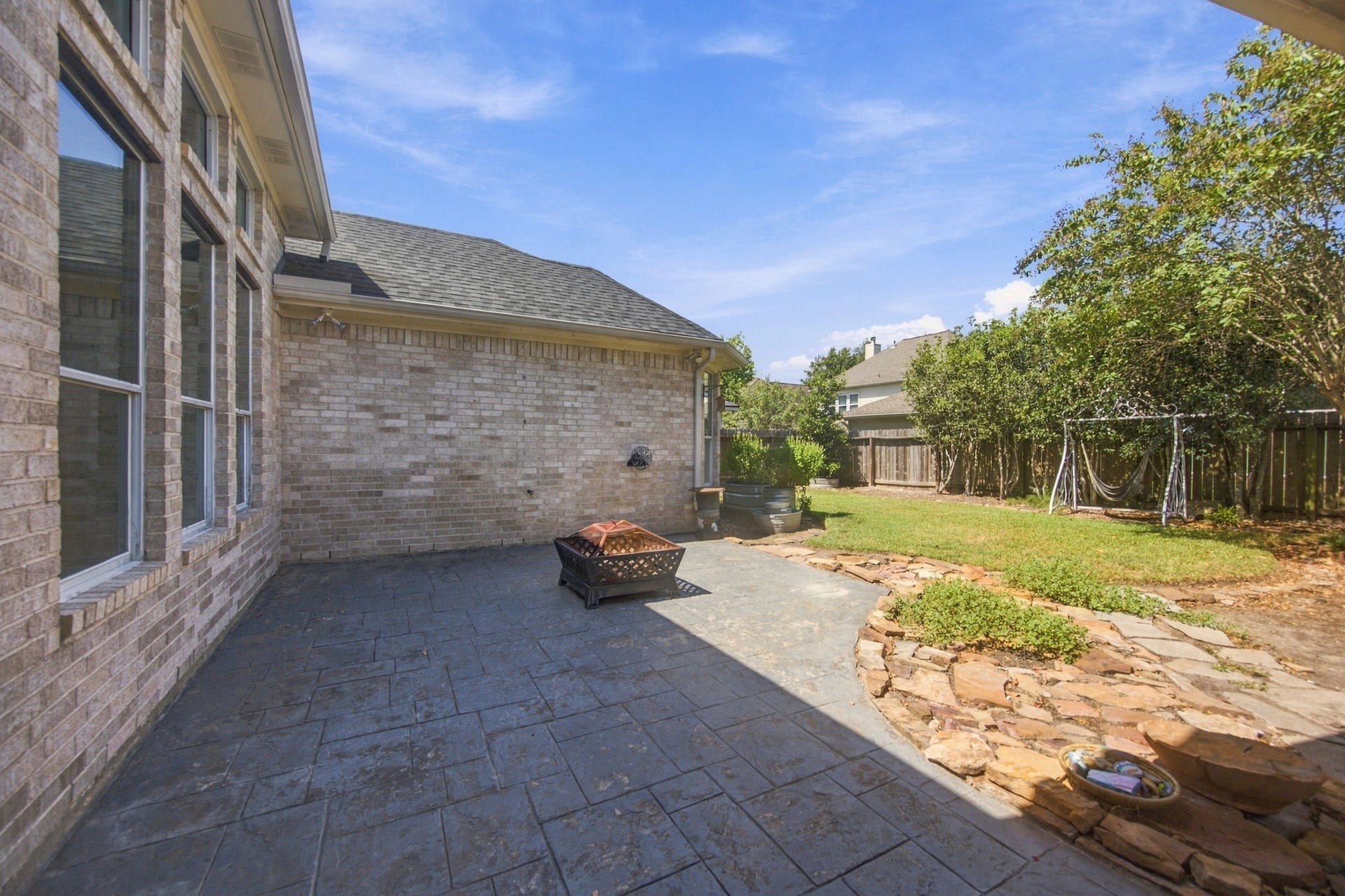 2417 La Rochelle Court, Seabrook, TX 77586 Spacious backyard patio with stone accents, perfect for outdoor gatherings, complemented by a lush lawn and mature trees for added privacy.