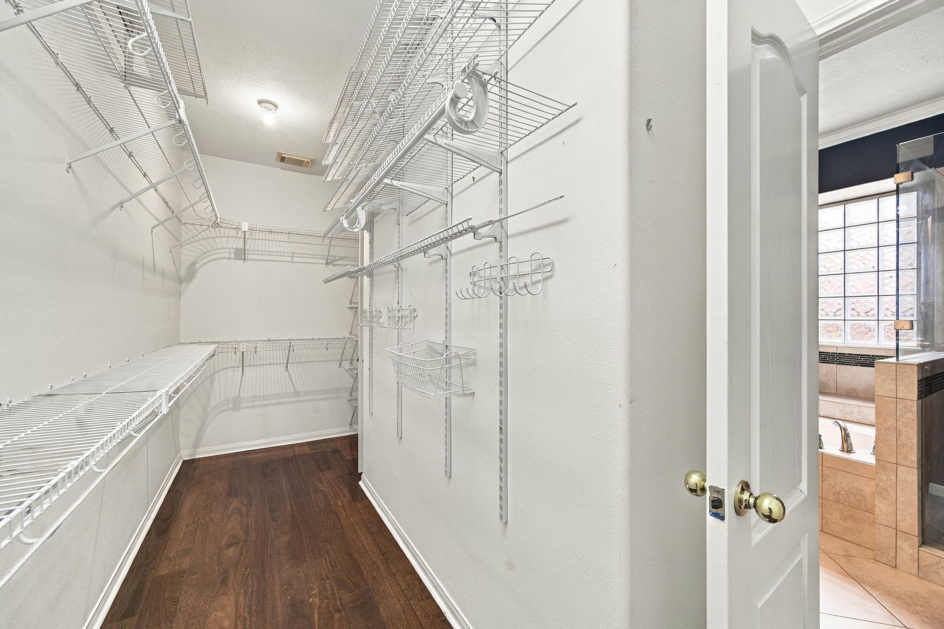 2417 La Rochelle Court, Seabrook, TX 77586 Spacious walk-in closet with ample shelving and hanging space, featuring sleek wooden flooring and easy access to the adjacent bathroom.