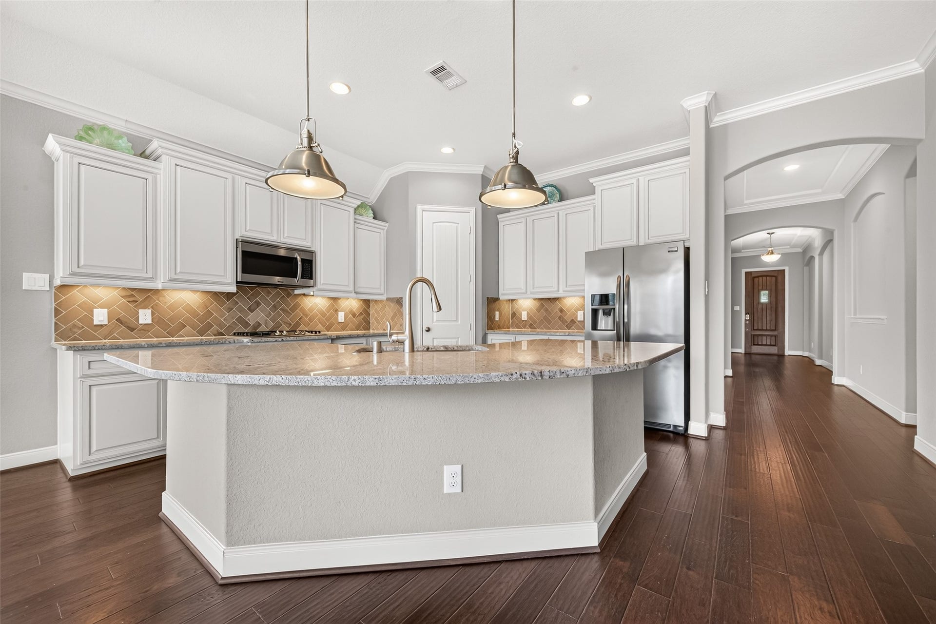 At the heart of the home is the open-concept kitchen featuring stainless steel appliances, 42-inch cabinetry, granite countertops, tile backsplash, and a large curved granite island. The kitchen flows seamlessly into the breakfast area and family room, creating an inviting space for everyday living and entertaining.