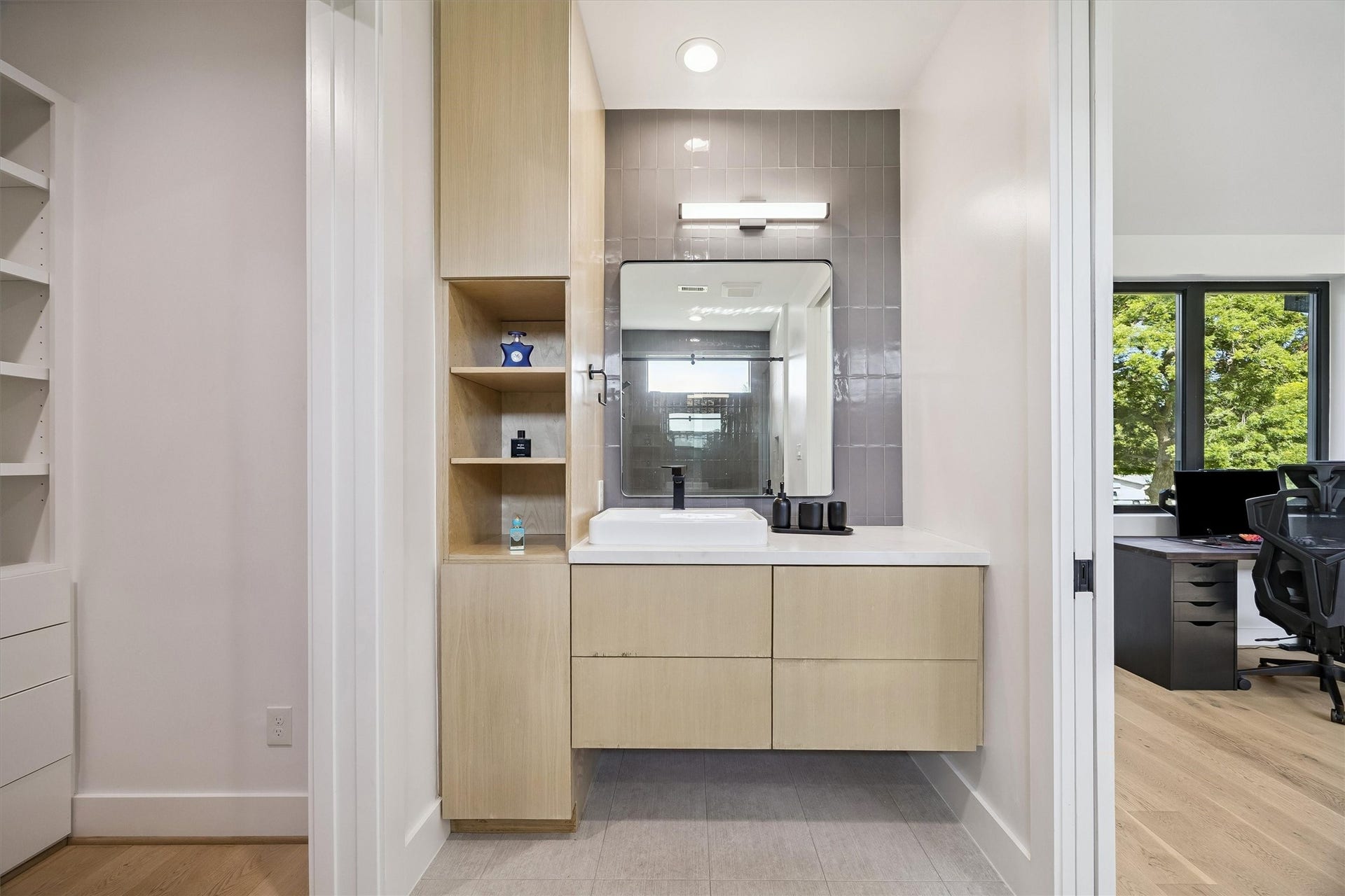 5210 Manor Drive, Sugar Land, TX 77479 Modern bathroom with sleek cabinetry, a large mirror, and stylish lighting, adjacent to a well-lit office space with large windows.