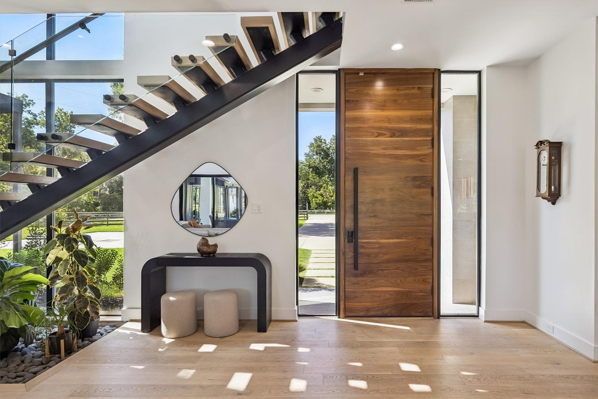 5210 Manor Drive, Sugar Land, TX 77479 Elegant entryway featuring a striking floating staircase, sleek wooden door, and modern decor, complemented by large windows that flood the space with natural light.