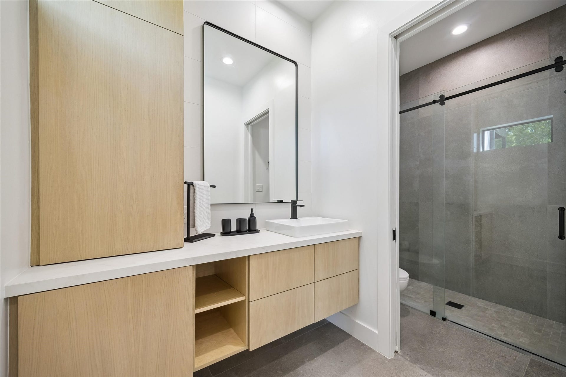 5210 Manor Drive, Sugar Land, TX 77479 Sleek modern bathroom featuring a floating vanity with light wood cabinetry, a large mirror, and a stylish vessel sink. The spacious walk-in shower includes elegant glass doors and contemporary fixtures.