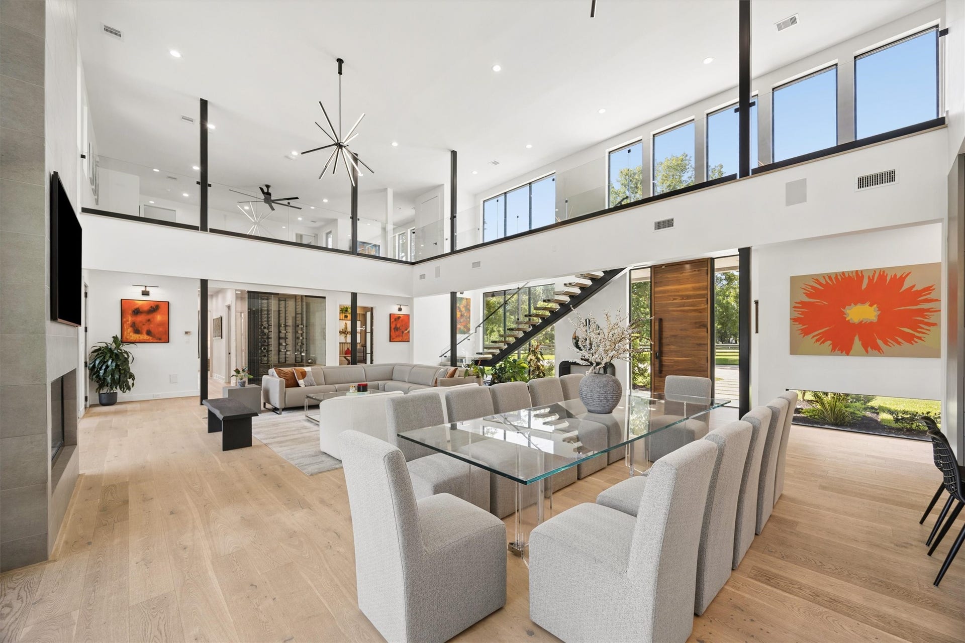 5210 Manor Drive, Sugar Land, TX 77479 Stunning modern living space with high ceilings, expansive windows, and an open floor plan. The room features a chic glass dining table, elegant contemporary furnishings, and a striking staircase leading to a loft area.