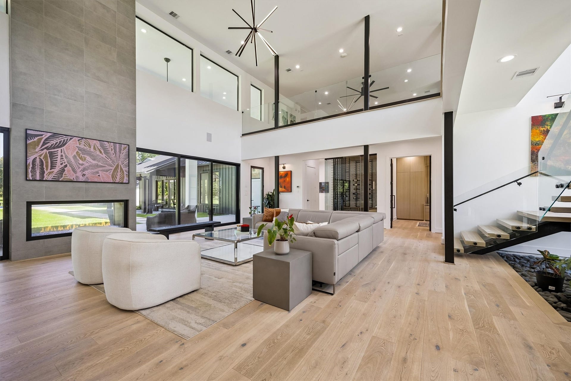 5210 Manor Drive, Sugar Land, TX 77479 Stunning modern living room with soaring ceilings, sleek fireplace, and expansive windows offering abundant natural light. Luxurious open-concept design features stylish furnishings and a contemporary staircase leading to a lofted area.