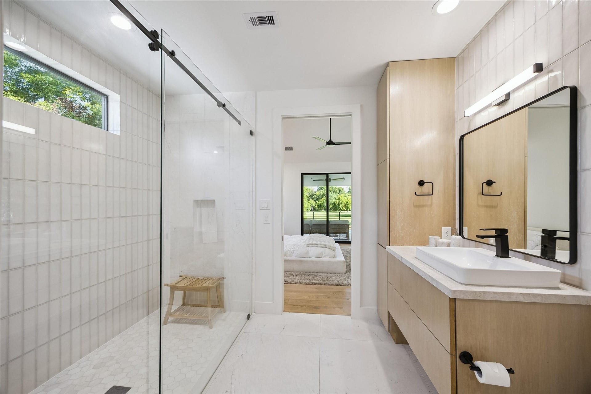 5210 Manor Drive, Sugar Land, TX 77479 Sleek modern bathroom with a glass-enclosed shower, stylish wood cabinetry, and a seamless transition to the bright, inviting bedroom beyond.
