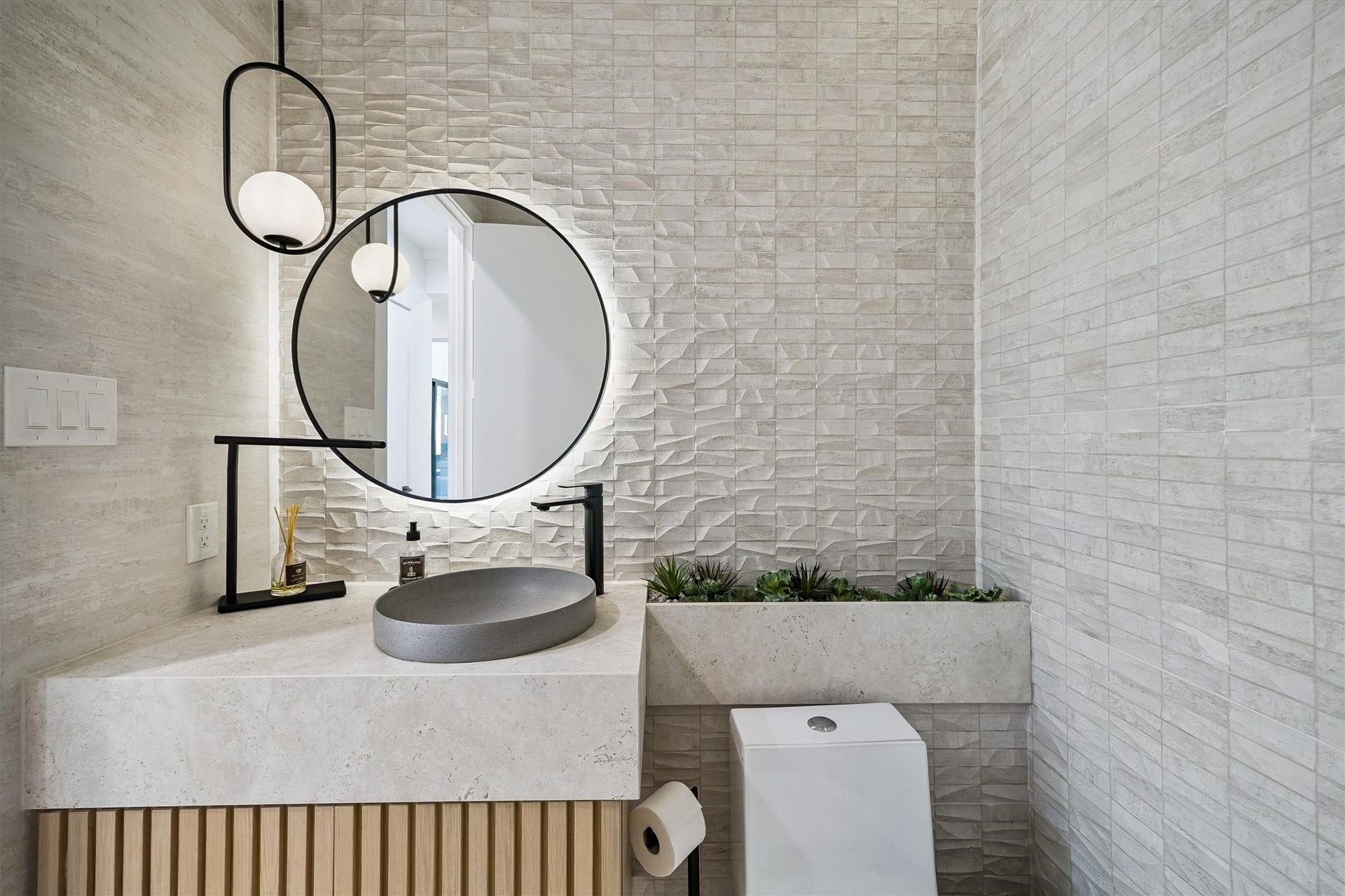 5210 Manor Drive, Sugar Land, TX 77479 Elegant modern bathroom featuring a textured accent wall, sleek round mirror, and contemporary fixtures with a stylish vessel sink and ambient lighting.